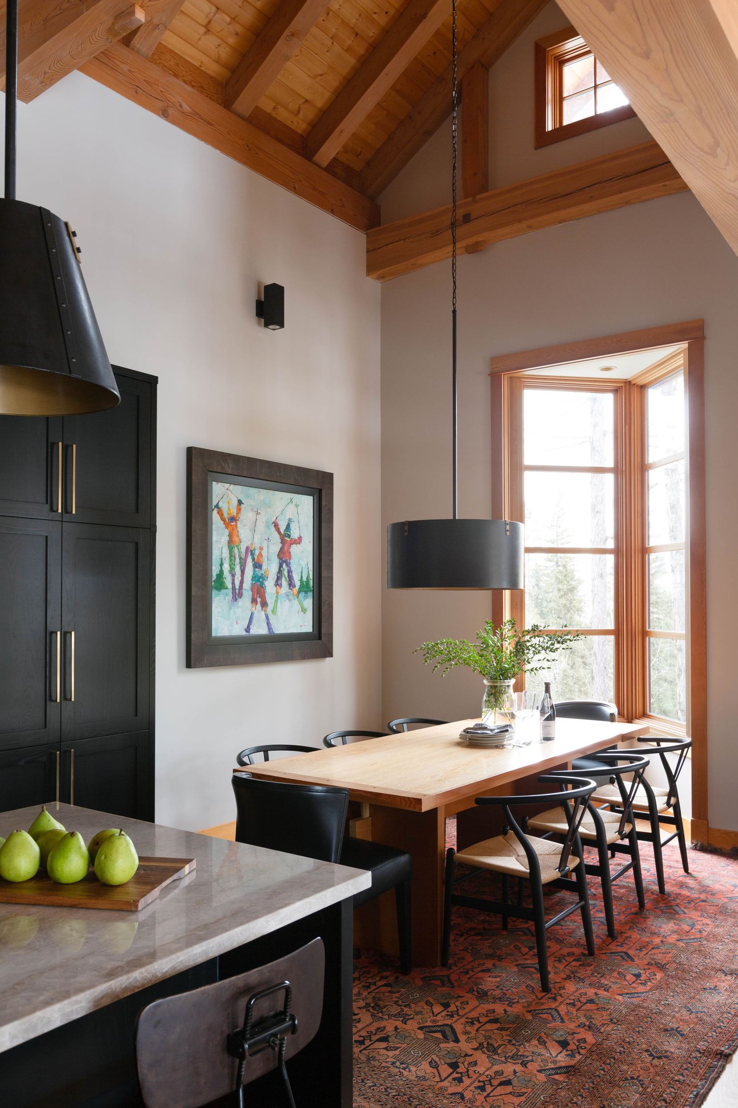 Vaulted wood ceiling dining area with black pendant lights, wishbone chairs, and colorful wall art.