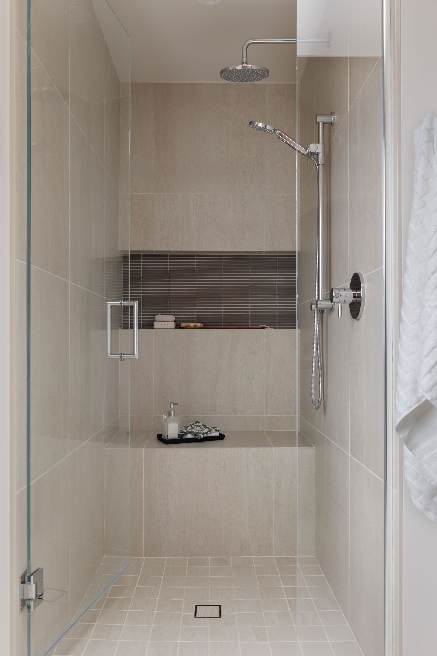 Elegant walk-in shower with beige tiles, rain showerhead, built-in niche shelf, and glass door.