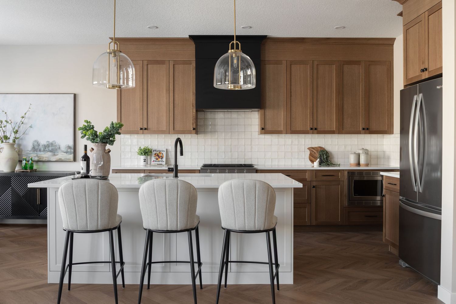 Warm transitional kitchen with walnut cabinets, white island, glass pendants, and herringbone wood floors.
