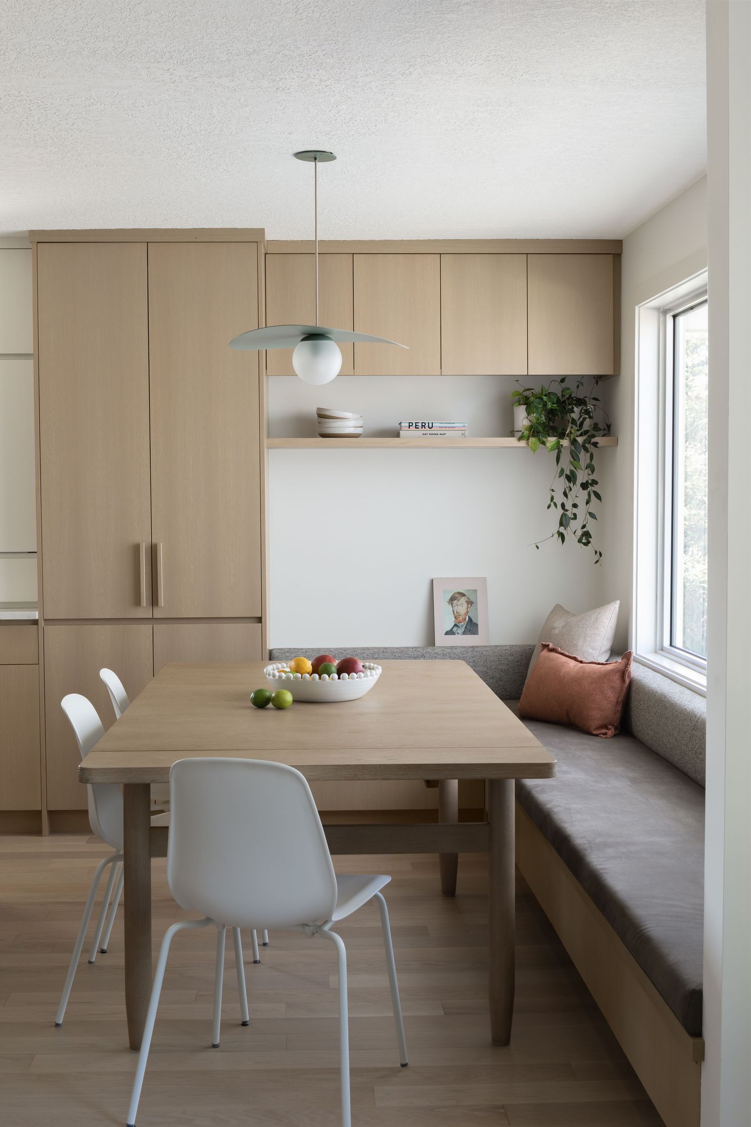 Minimalist dining nook with light wood cabinets, built-in bench, pendant light, and white chairs.