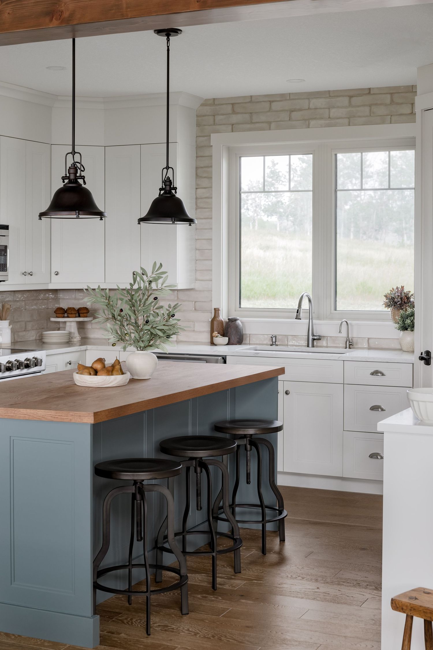 Bright farmhouse kitchen with white cabinets, blue island, butcher block countertop, and black pendant lights.