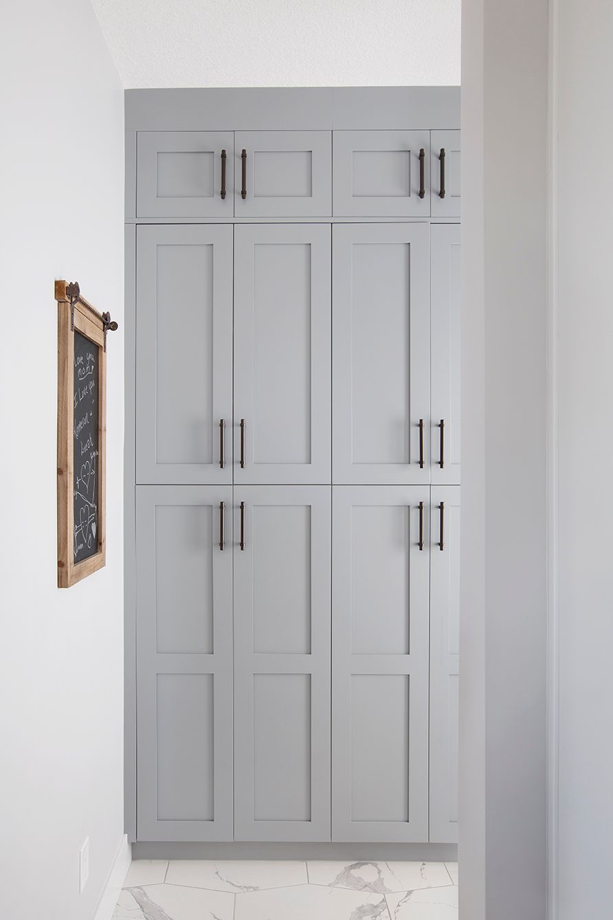 Floor-to-ceiling gray shaker built-in storage cabinets with bronze hardware on white marble tile floor.