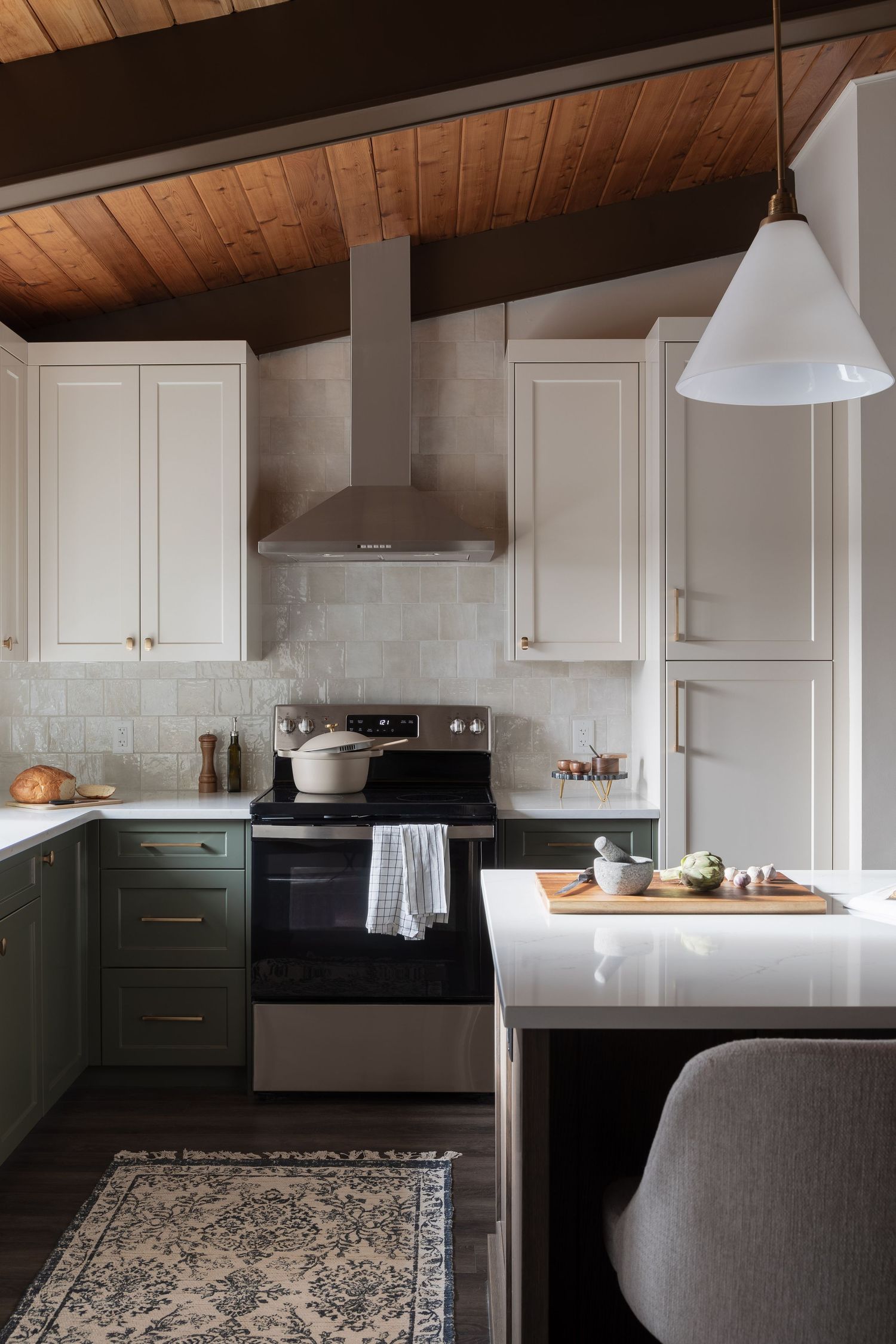 Two-tone kitchen with sage lower cabinets, white uppers, wood ceiling, subway tile backsplash, and range hood.