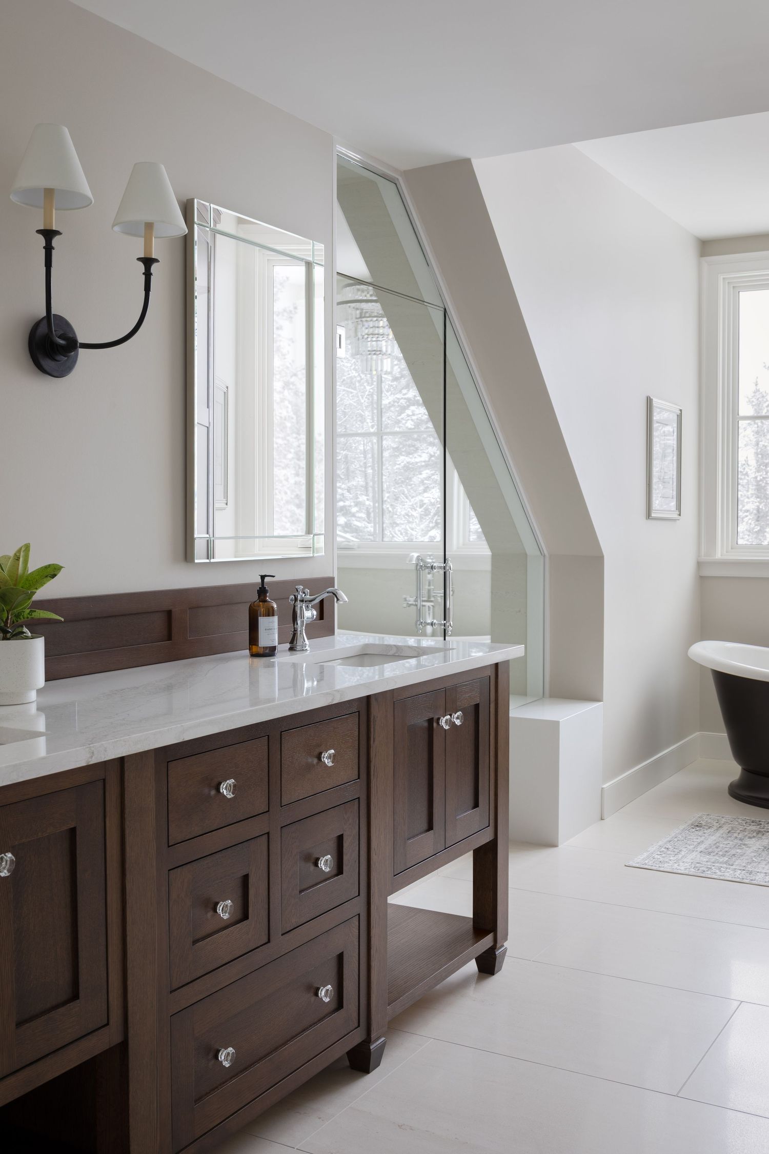 Dark wood double vanity with marble countertop, silver mirror, and black clawfoot tub in attic bathroom.