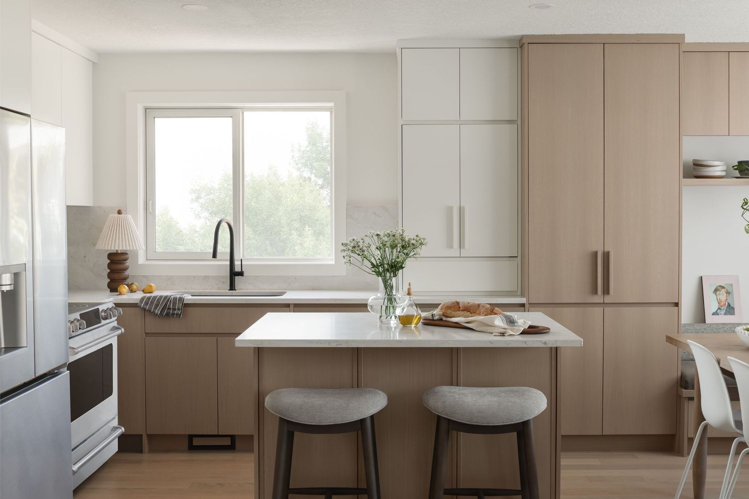 Modern kitchen with taupe flat-panel cabinets, white island, bar stools, and large window above sink.