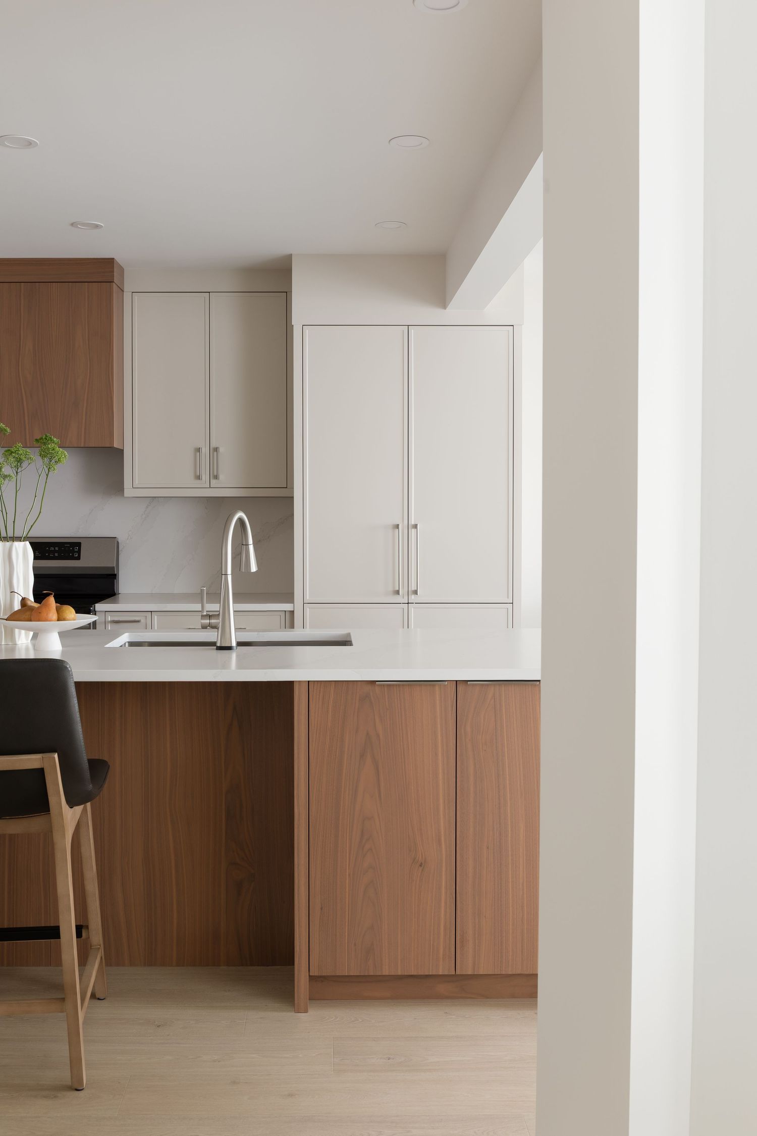 Modern kitchen with two-tone walnut and white cabinetry, island with sink, and light hardwood floors.