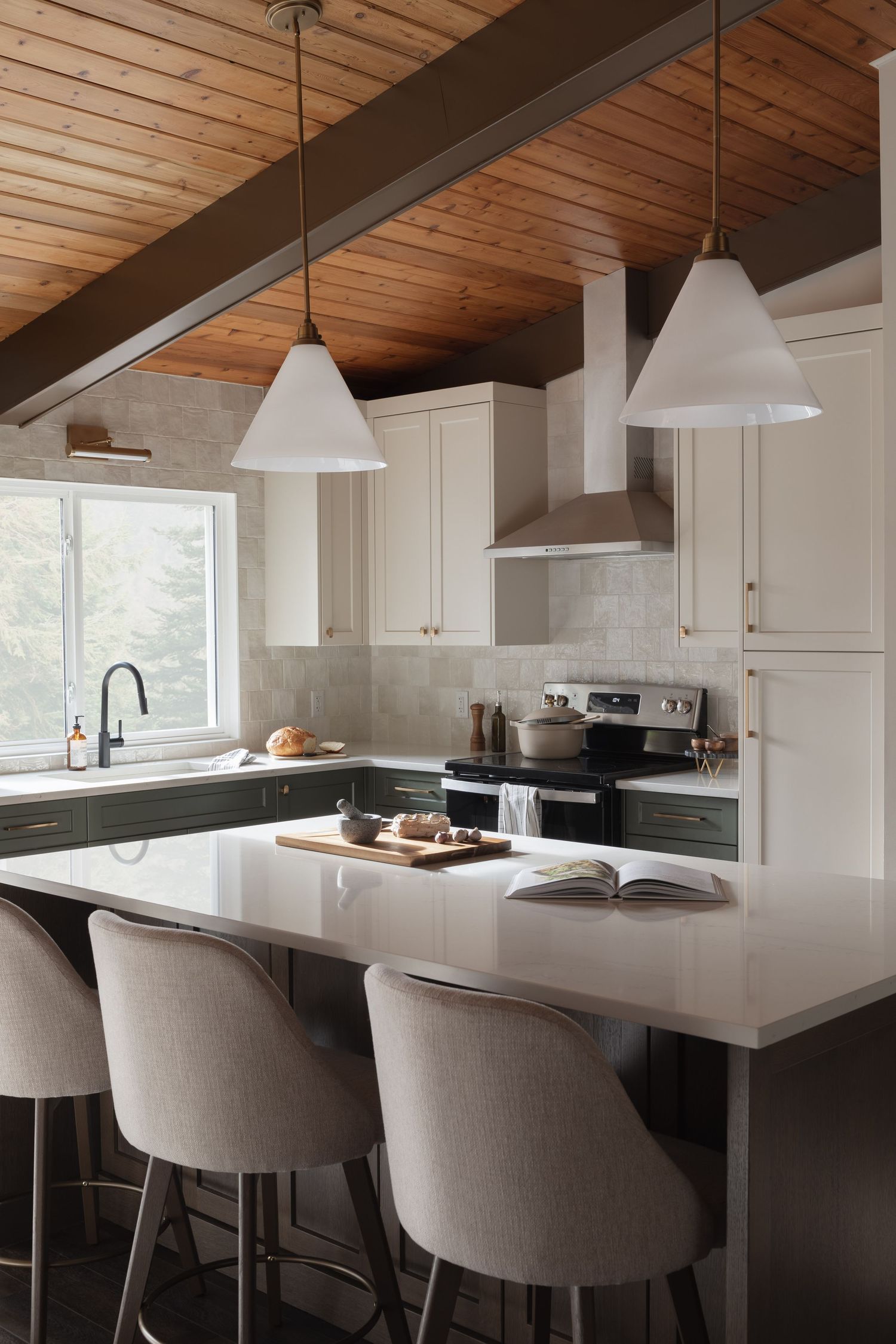 Stylish kitchen featuring wood ceiling beams, two-tone green and white cabinets, white pendants, and island seating.