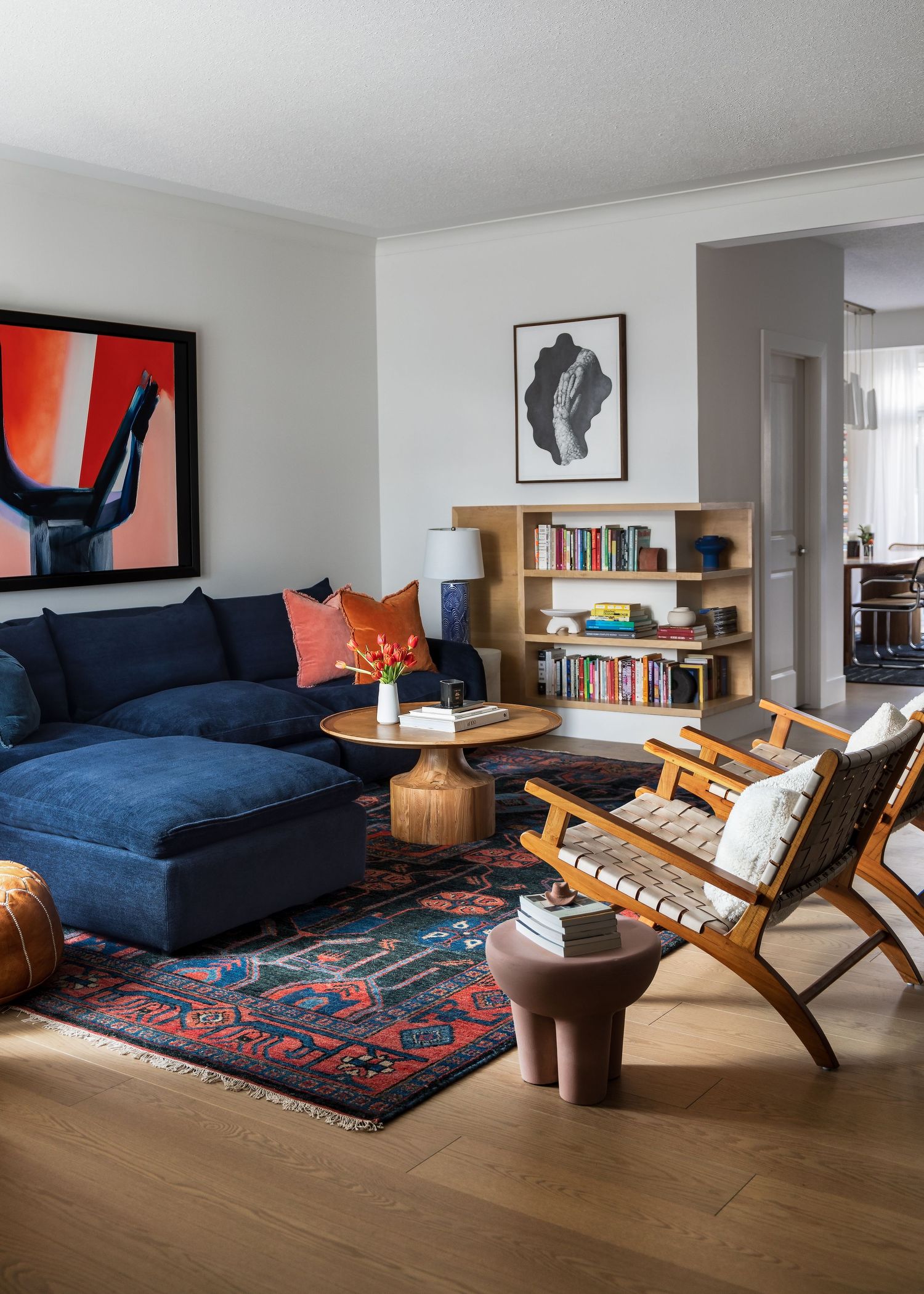 Eclectic living room with navy blue sectional sofa, bold red artwork, vintage rug, and wood bookshelf.
