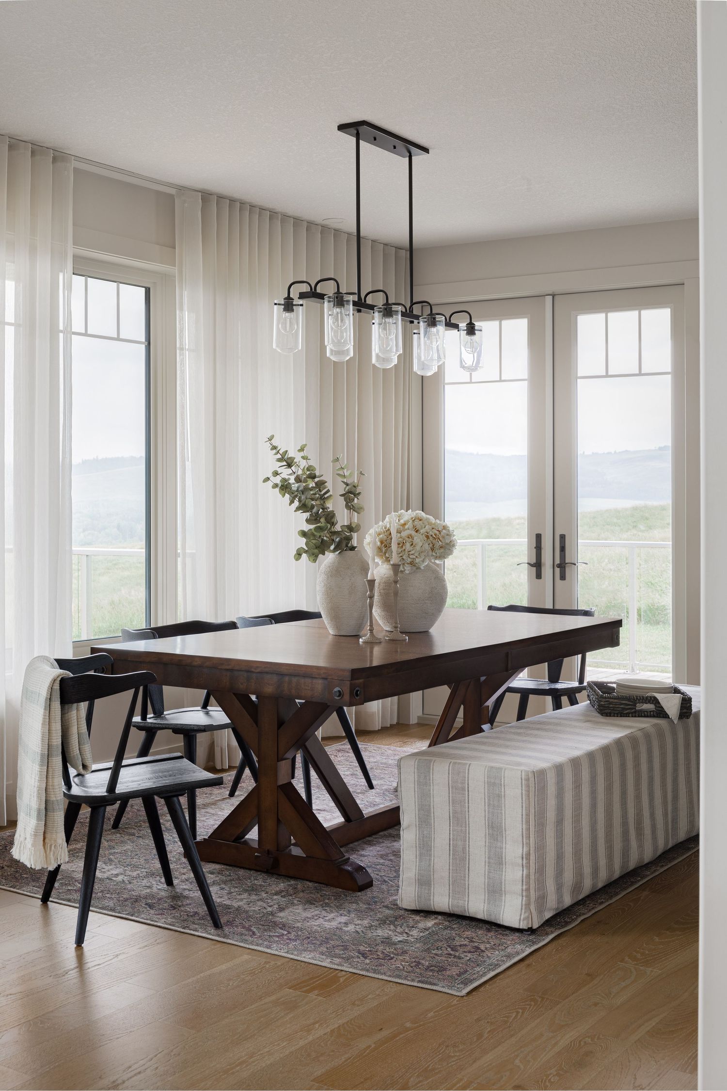 Farmhouse dining room with rustic wood table, striped bench, black chairs, and glass pendant chandelier.