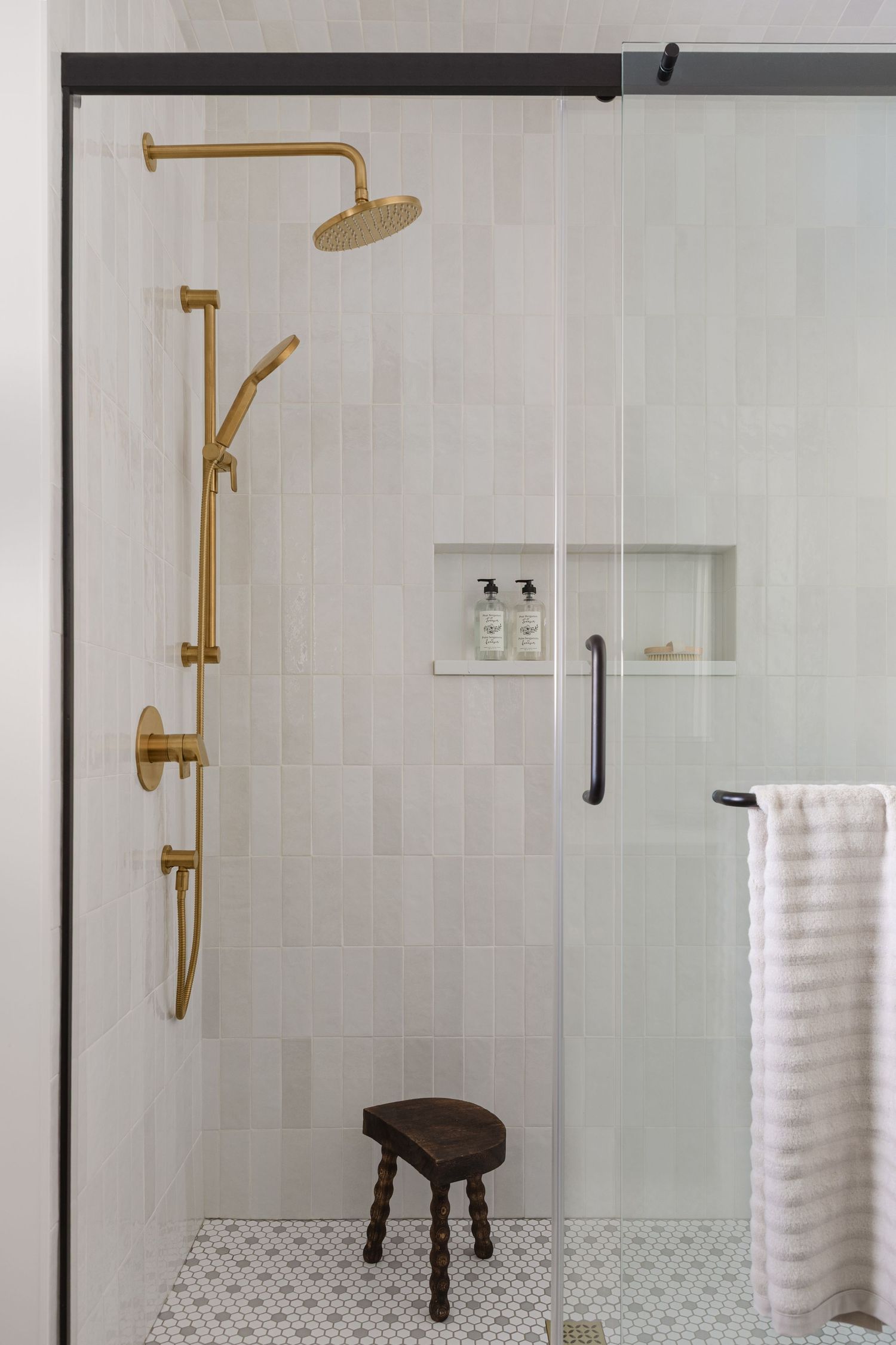 Elegant walk-in shower with gold brass fixtures, white subway tiles, and wooden stool, by Calgary Interior photographer Rebecca Frick.