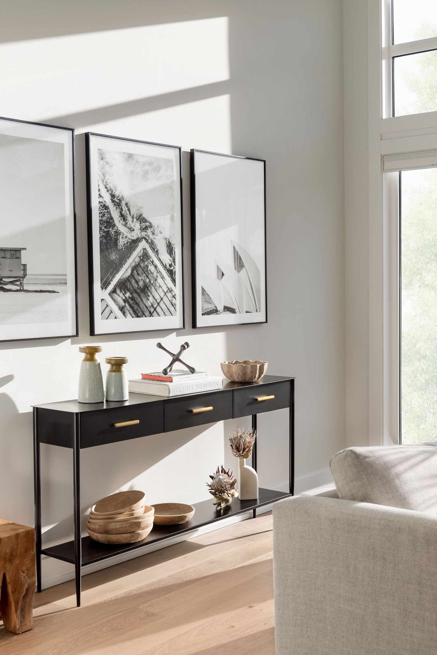 Black console table with gold hardware, black-and-white photography gallery wall, and decorative accessories in bright room.