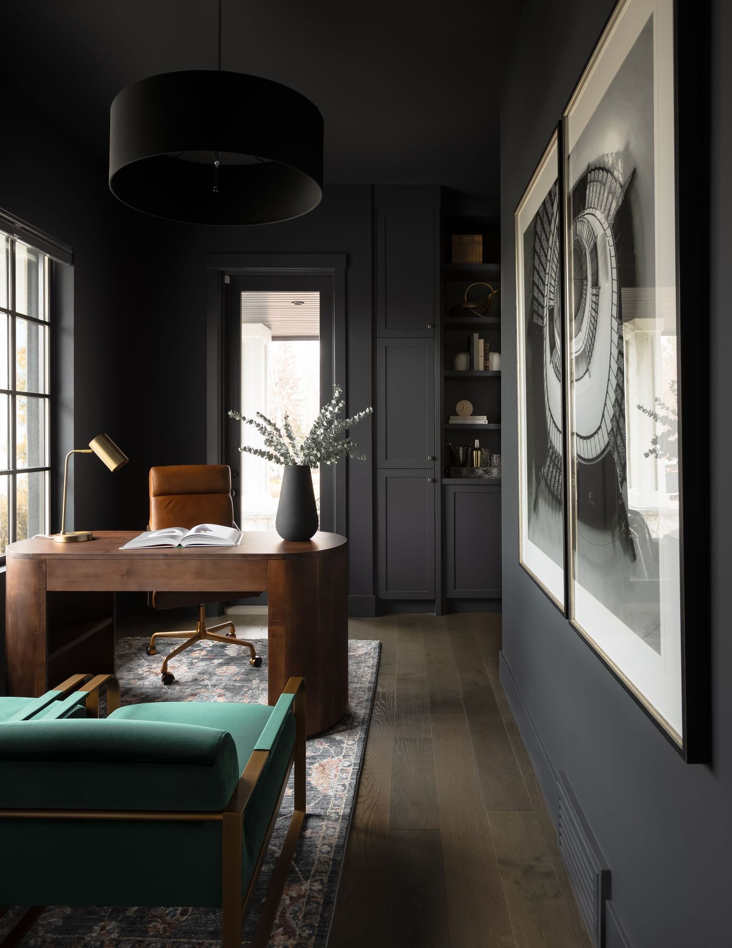 Dramatic dark home office with black walls, walnut desk, leather chair, and large framed artwork.
