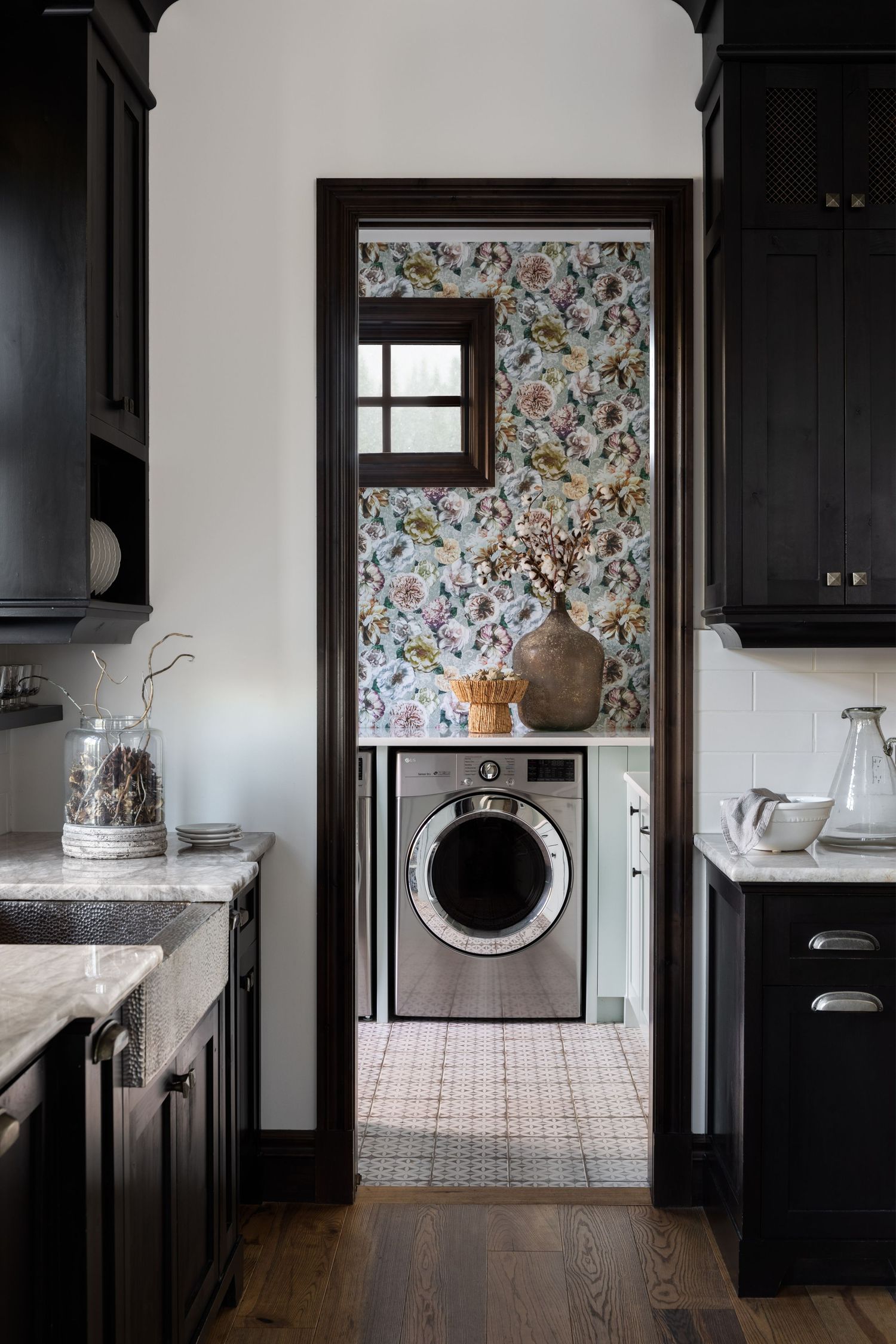 Dark kitchen doorway framing a floral wallpaper laundry room with front-load washer and patterned tile floor.