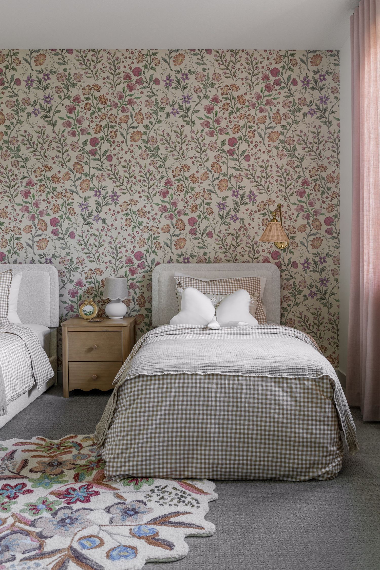 Charming girls bedroom with floral wallpaper, twin beds, gingham duvet, and botanical shaped area rug.