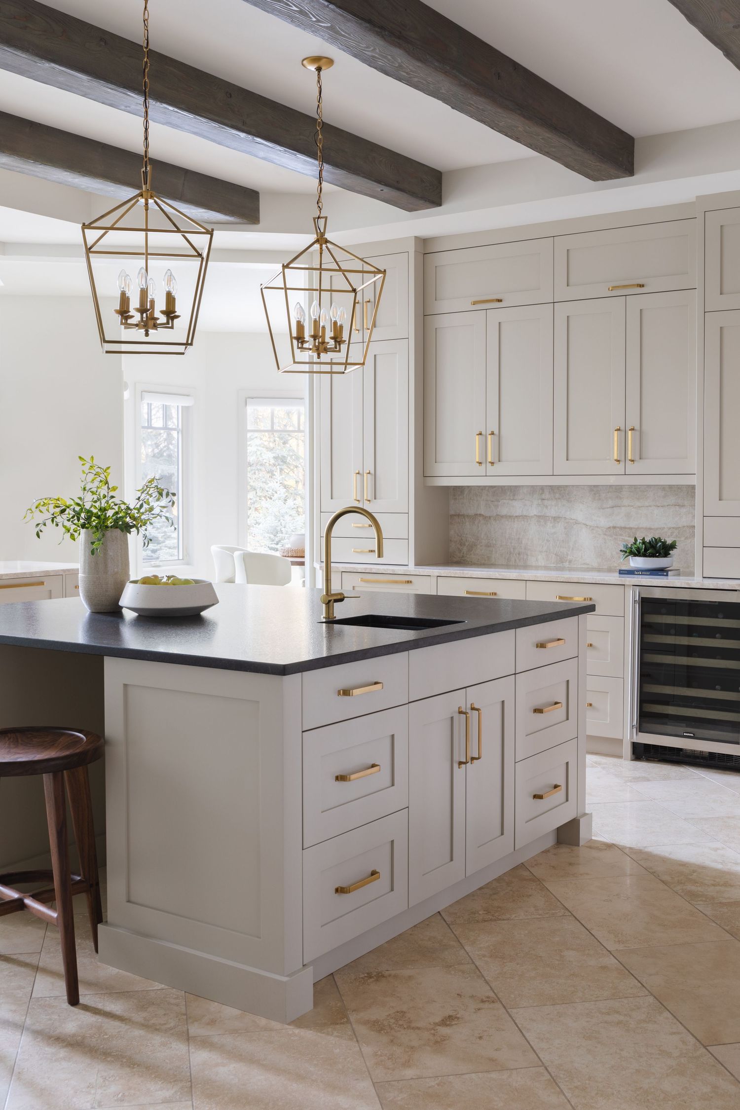 Transitional kitchen with cream cabinets, black island countertop, brass hardware, lantern pendants, and exposed wood ceiling beams.