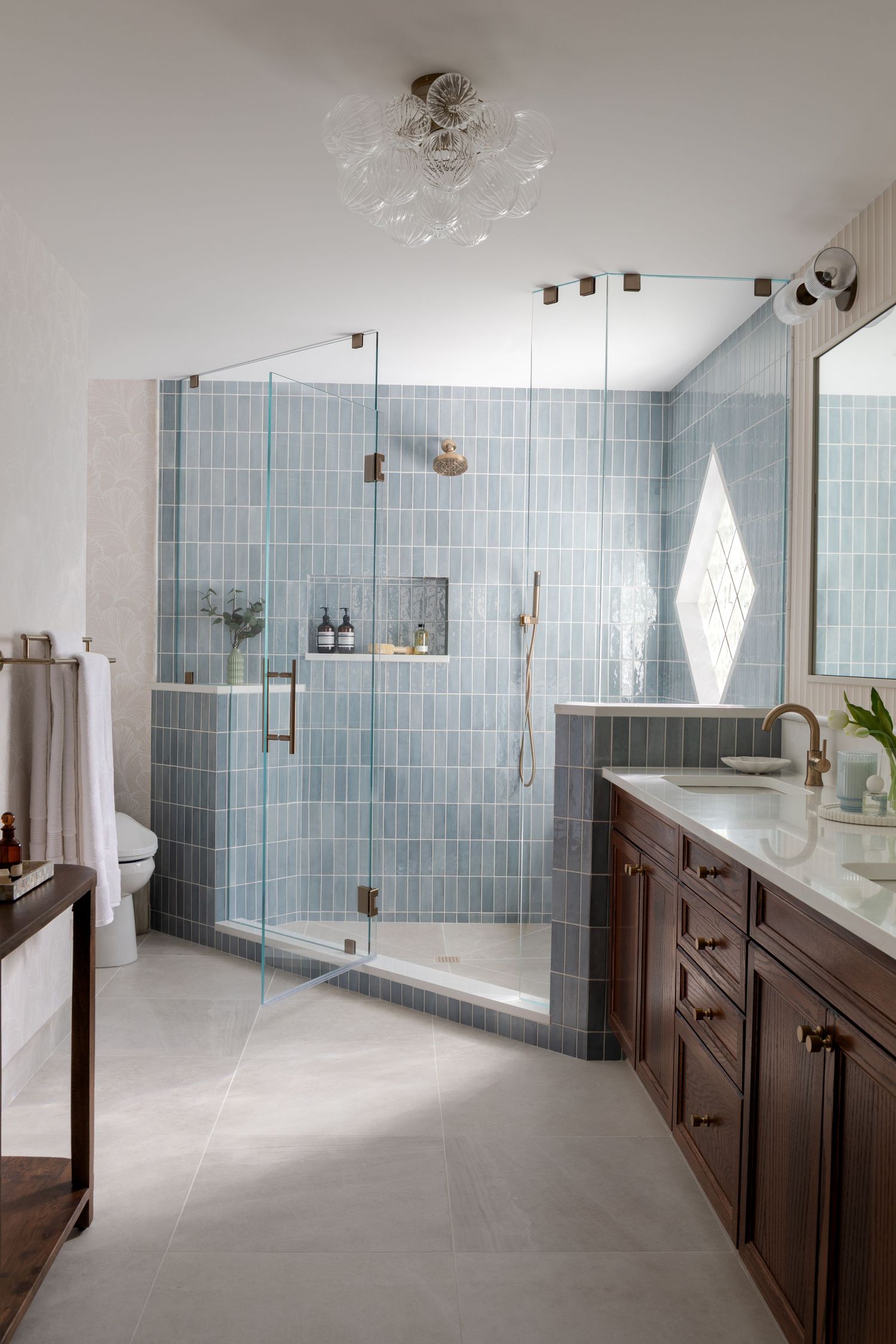 Modern bathroom with blue subway tile walk-in shower, dark wood vanity, white marble countertop, and glass enclosure.