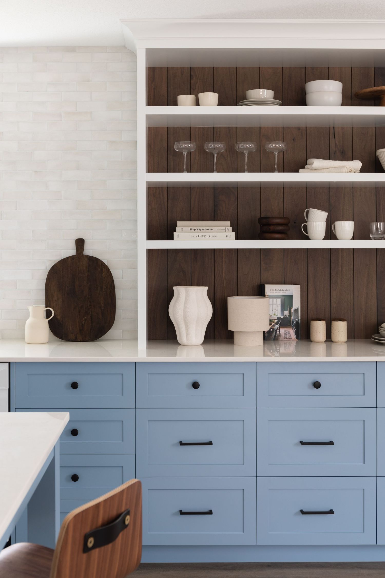 Blue shaker cabinets with black hardware, open shelving on dark wood backing displaying white ceramics.