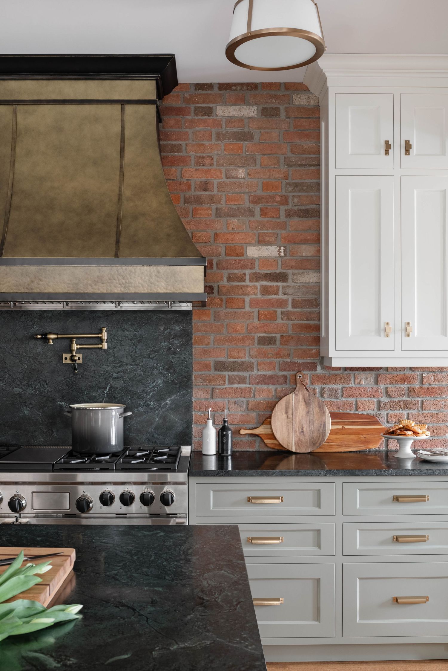 Luxury kitchen with brass range hood, soapstone counters, brick backsplash, and white upper cabinets.