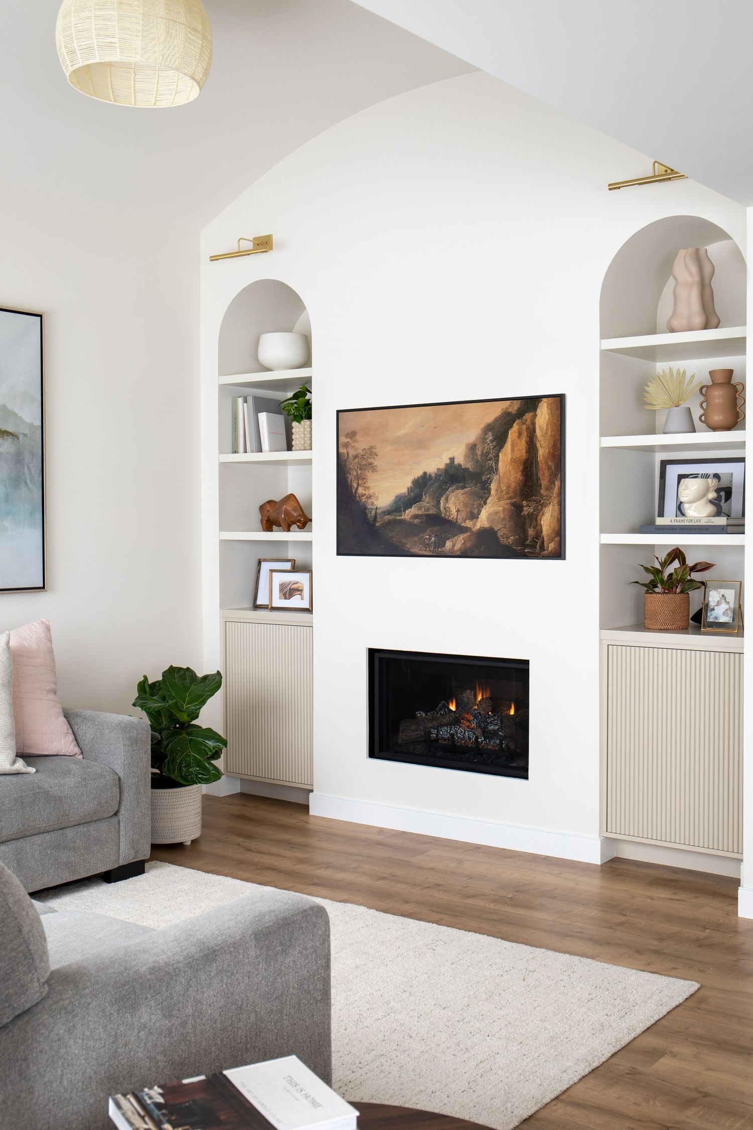 Bright living room with arched built-in shelves, gas fireplace, Samsung Frame TV, and vaulted white ceiling.