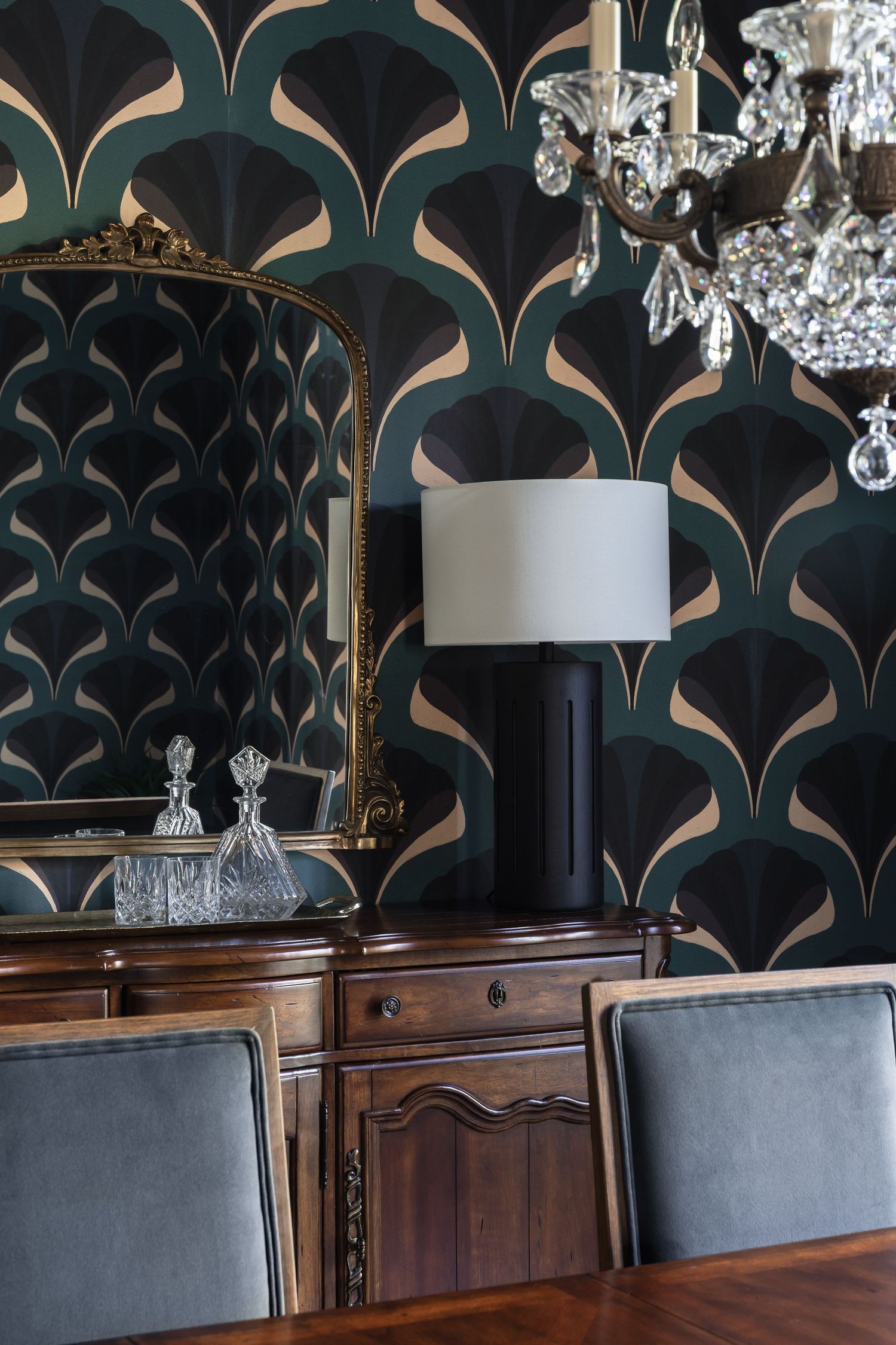 Elegant sideboard with gold mirror and lamp against bold dark Art Deco patterned wallpaper.