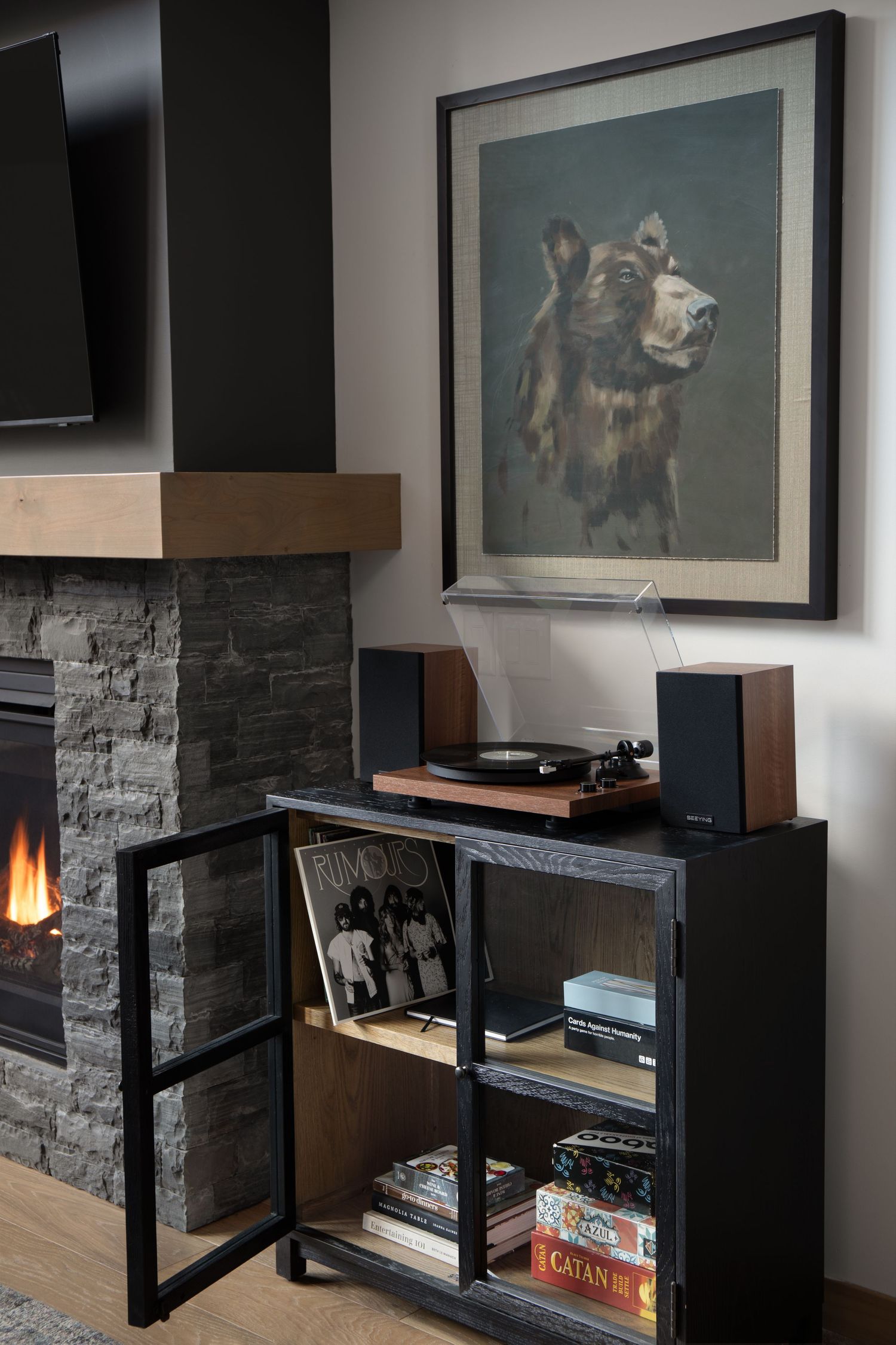 Vinyl record player on black cabinet beside stone fireplace with wolf portrait artwork above.
