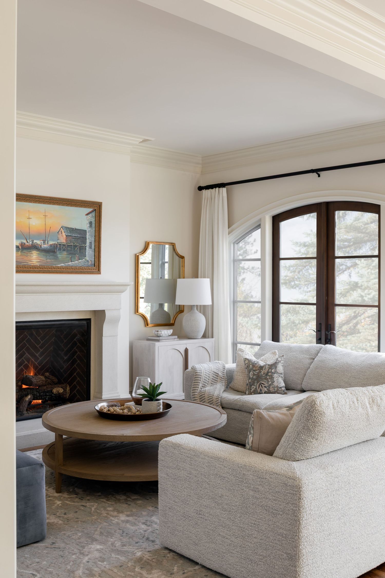 Bright living room with cream sofa, herringbone fireplace, round coffee table, and arched French doors.