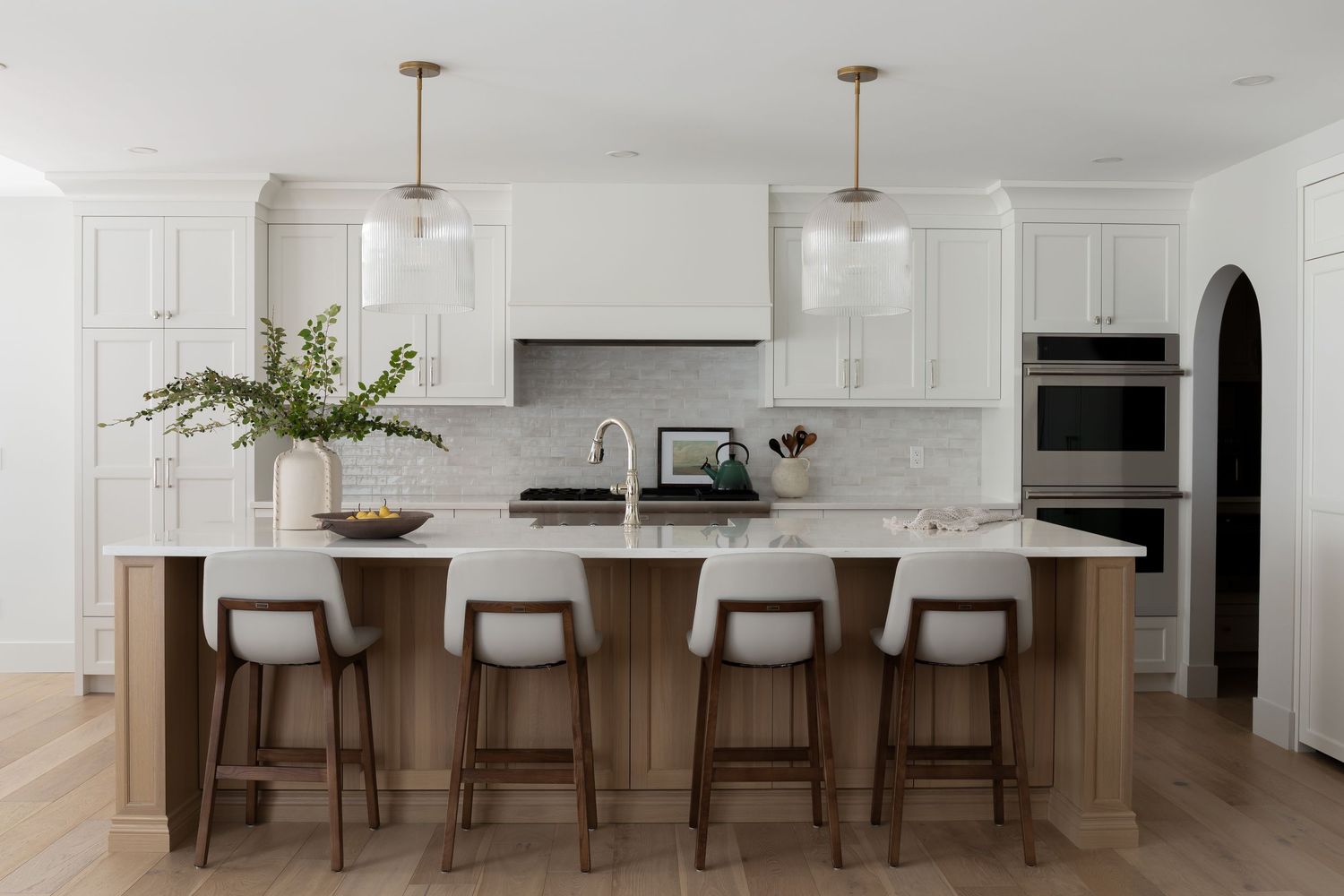 Bright white kitchen with large wood island, bar stools, glass pendants, and shaker cabinets, by Calgary Interior photographer Rebecca Frick