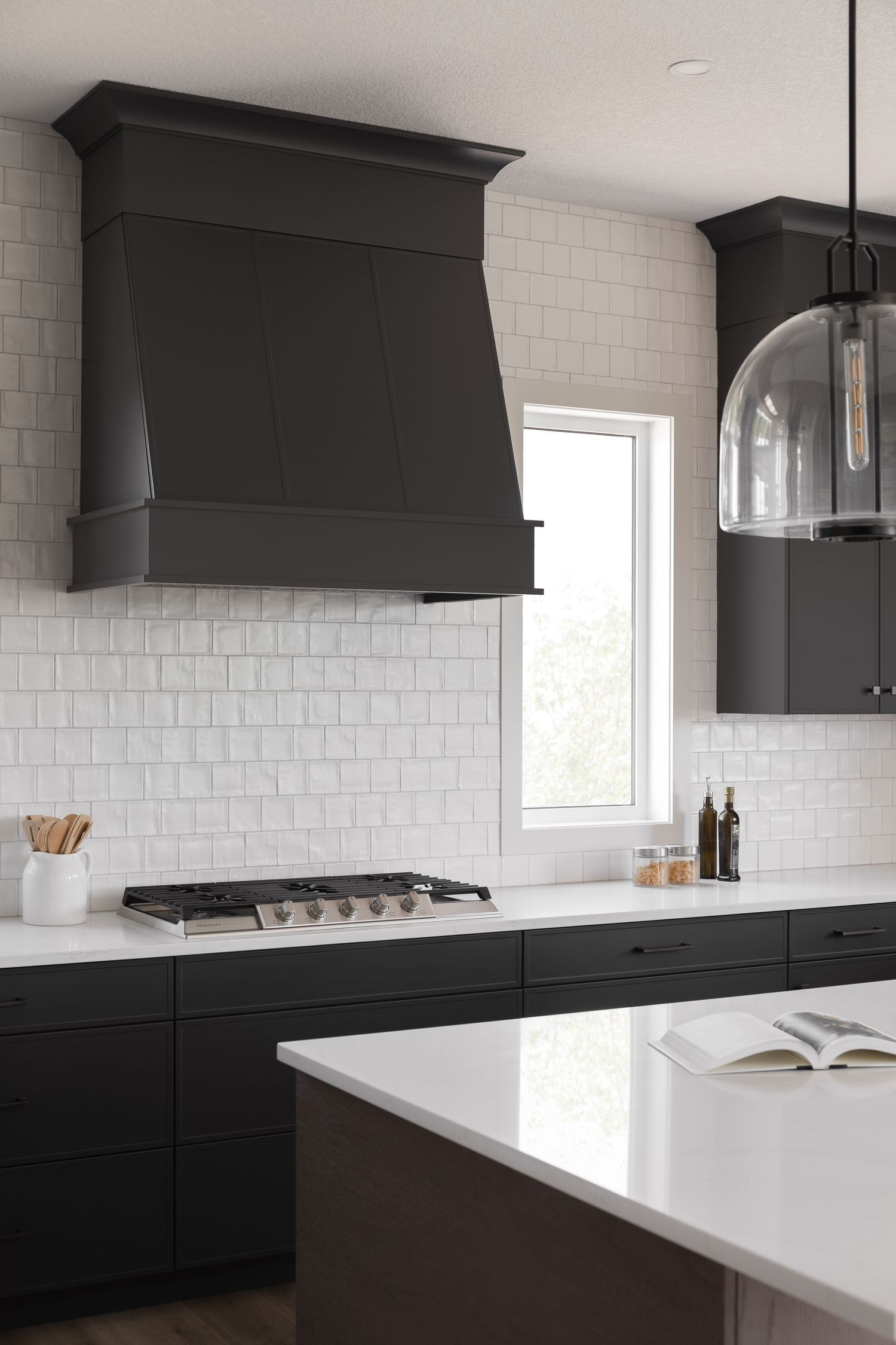 Modern kitchen with dark cabinets, white subway tile backsplash, gas cooktop, and black range hood.