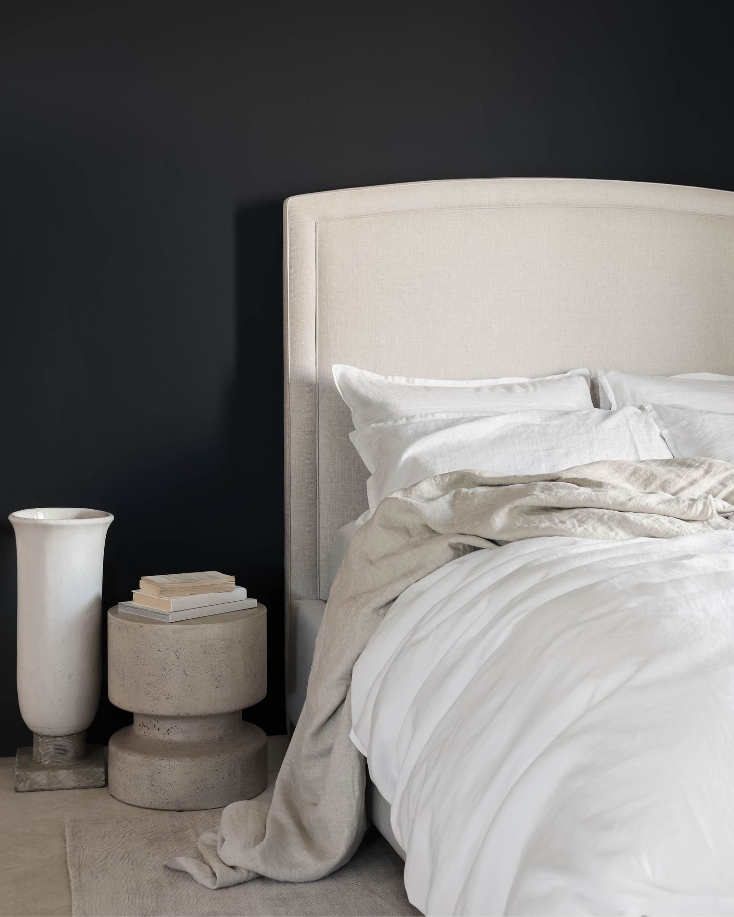 Minimalist bedroom with cream upholstered headboard, white bedding, and dark charcoal wall.