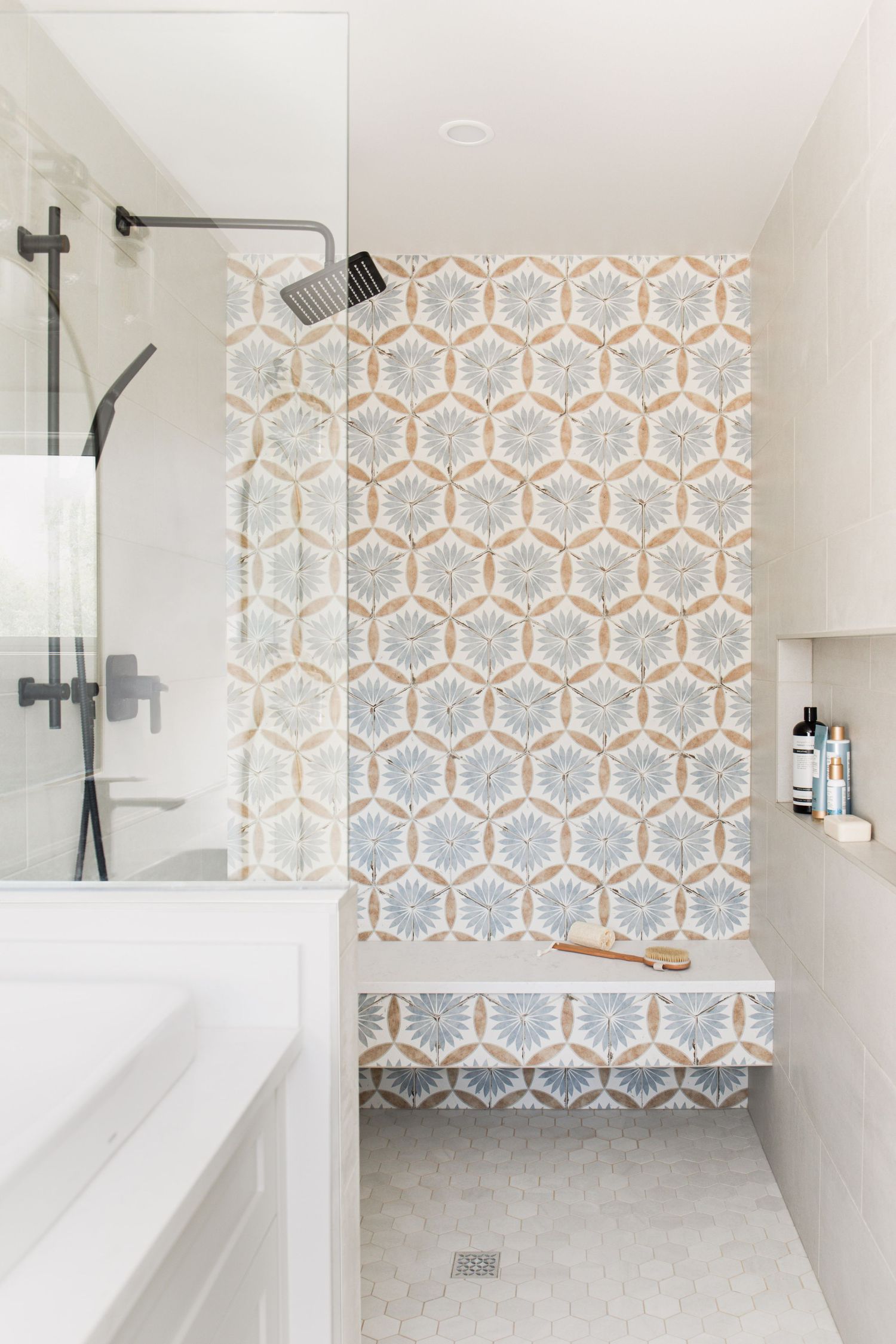 Modern shower with decorative hexagonal floral patterned tile accent wall, built-in bench, and matte black fixtures.