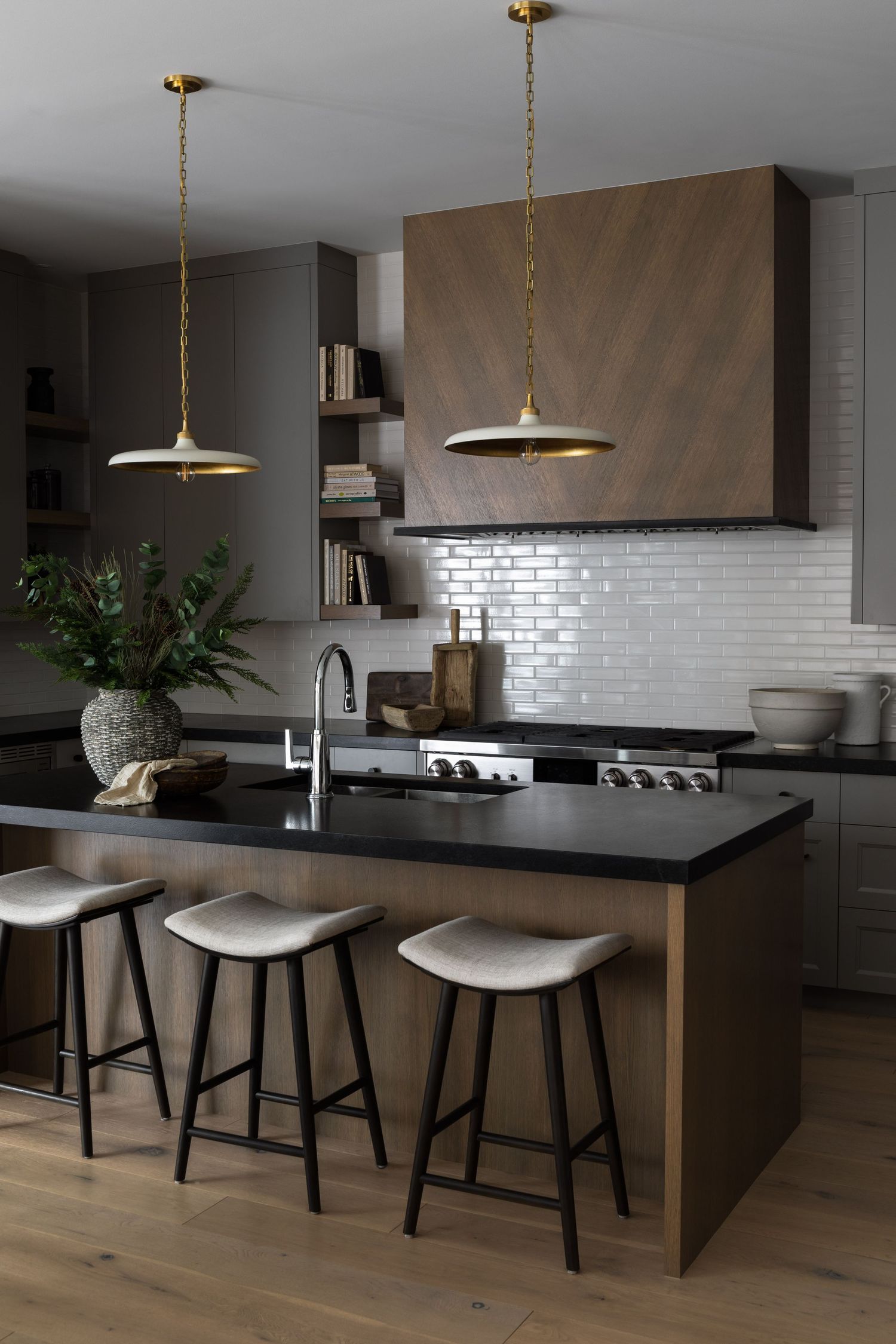 Modern kitchen with dark wood island, black countertops, white subway tile, and brass pendant lights.