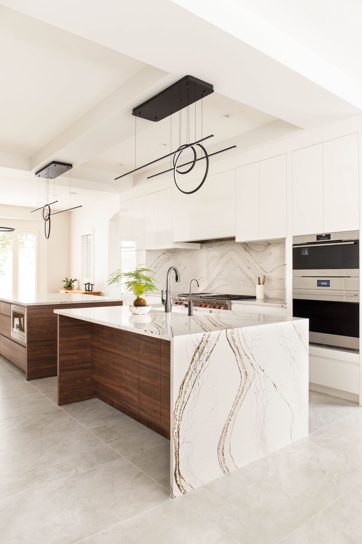 Luxury modern kitchen with marble waterfall island, dark wood cabinets, white upper cabinets, and contemporary pendant lights.