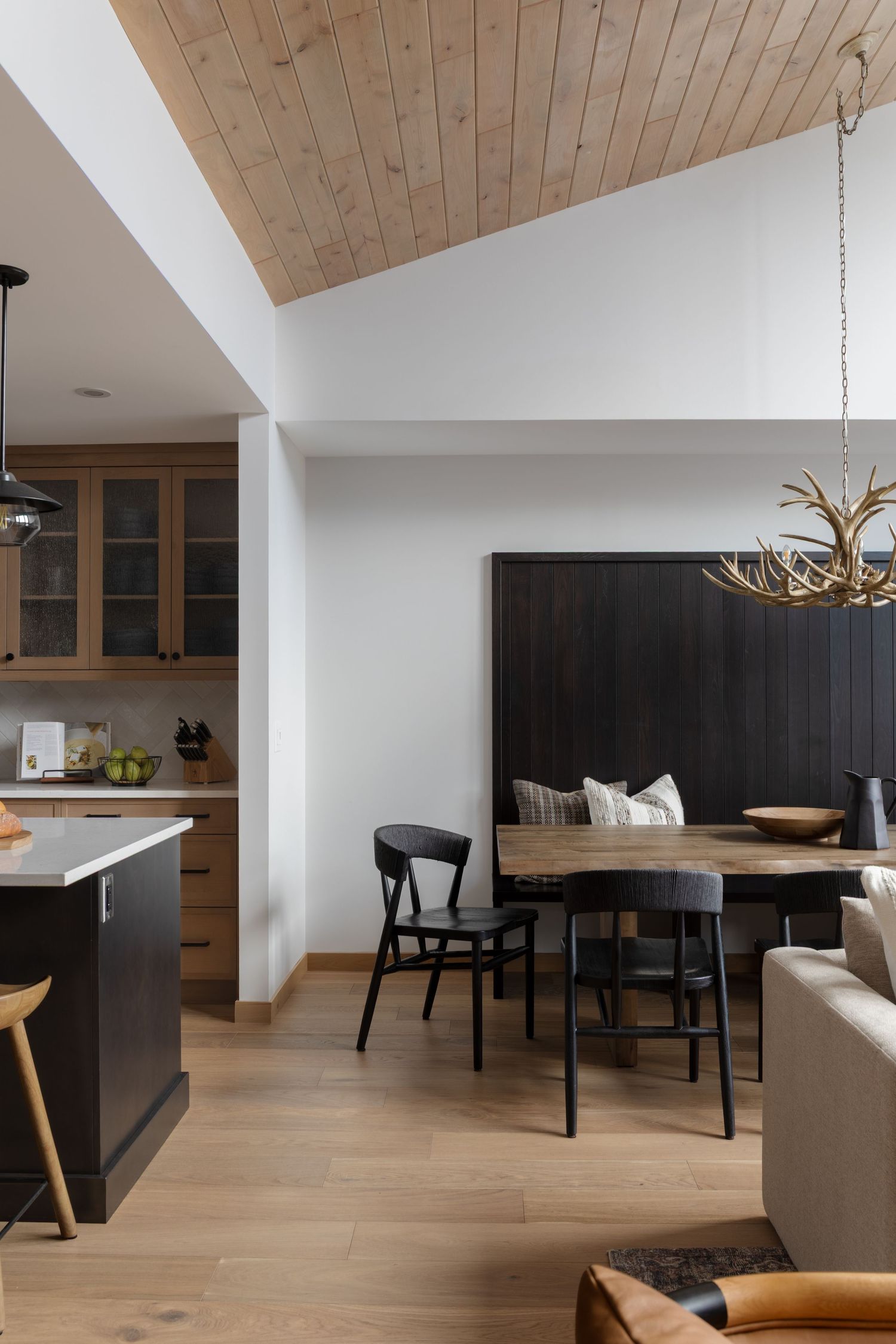 Open concept dining area with antler chandelier, black banquette, and vaulted ceiling, by Calgary Interior photographer Rebecca Frick.