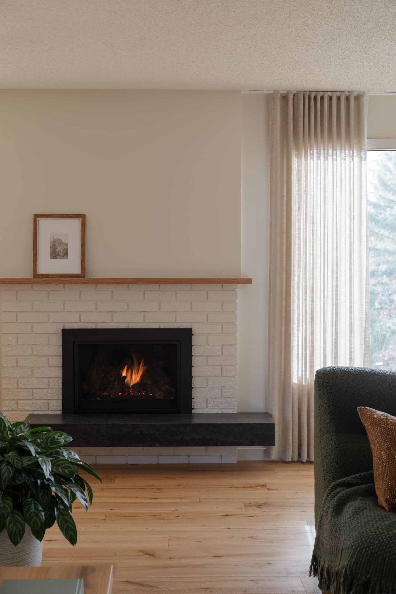 White brick fireplace with wood mantel and framed art in a minimalist living room with hardwood floors.