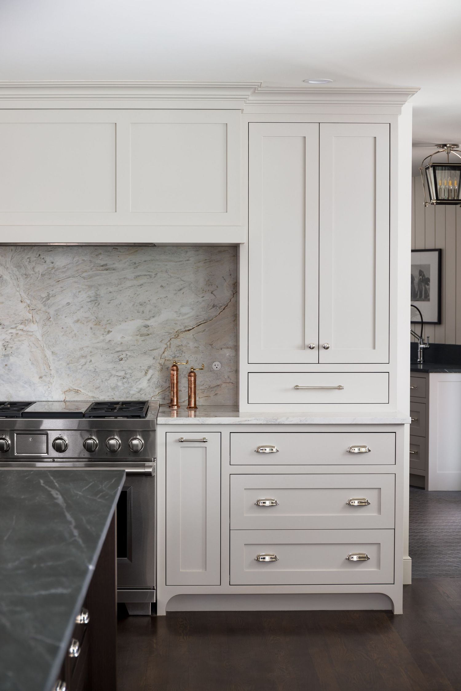White shaker kitchen cabinets with silver hardware, marble backsplash, and stainless steel range in elegant kitchen.