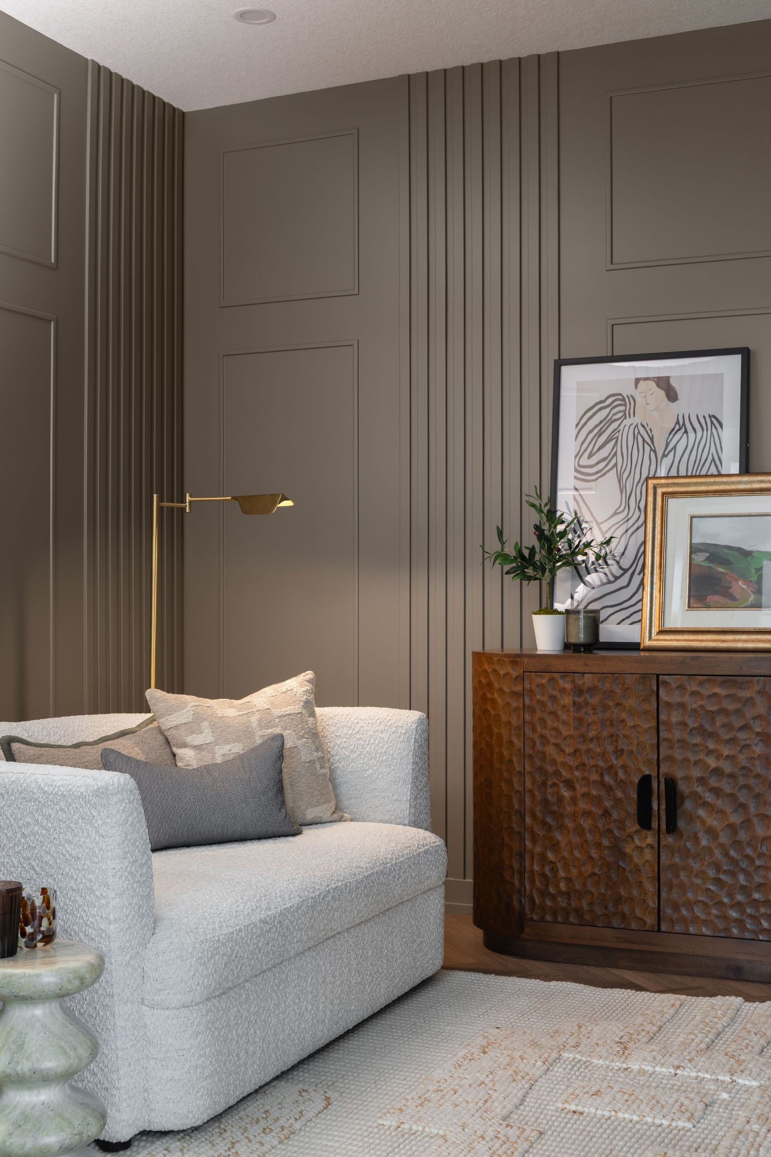 Elegant living room with olive green paneled wall, white textured sofa, brass floor lamp, and carved wood cabinet.