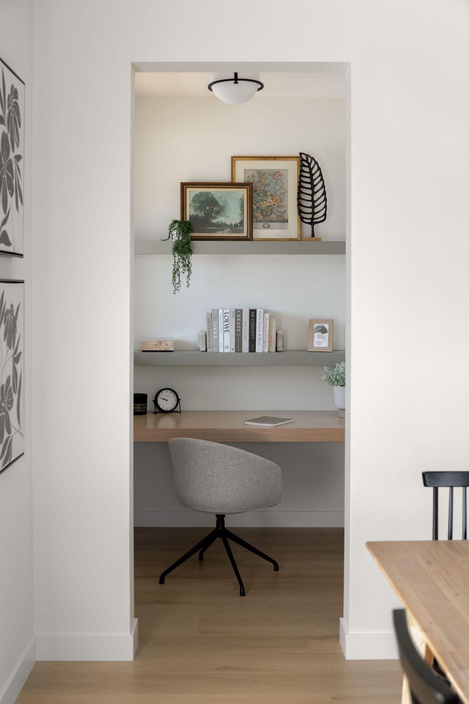Compact home office nook with floating shelves, wood desk, gray swivel chair, and decorative art.