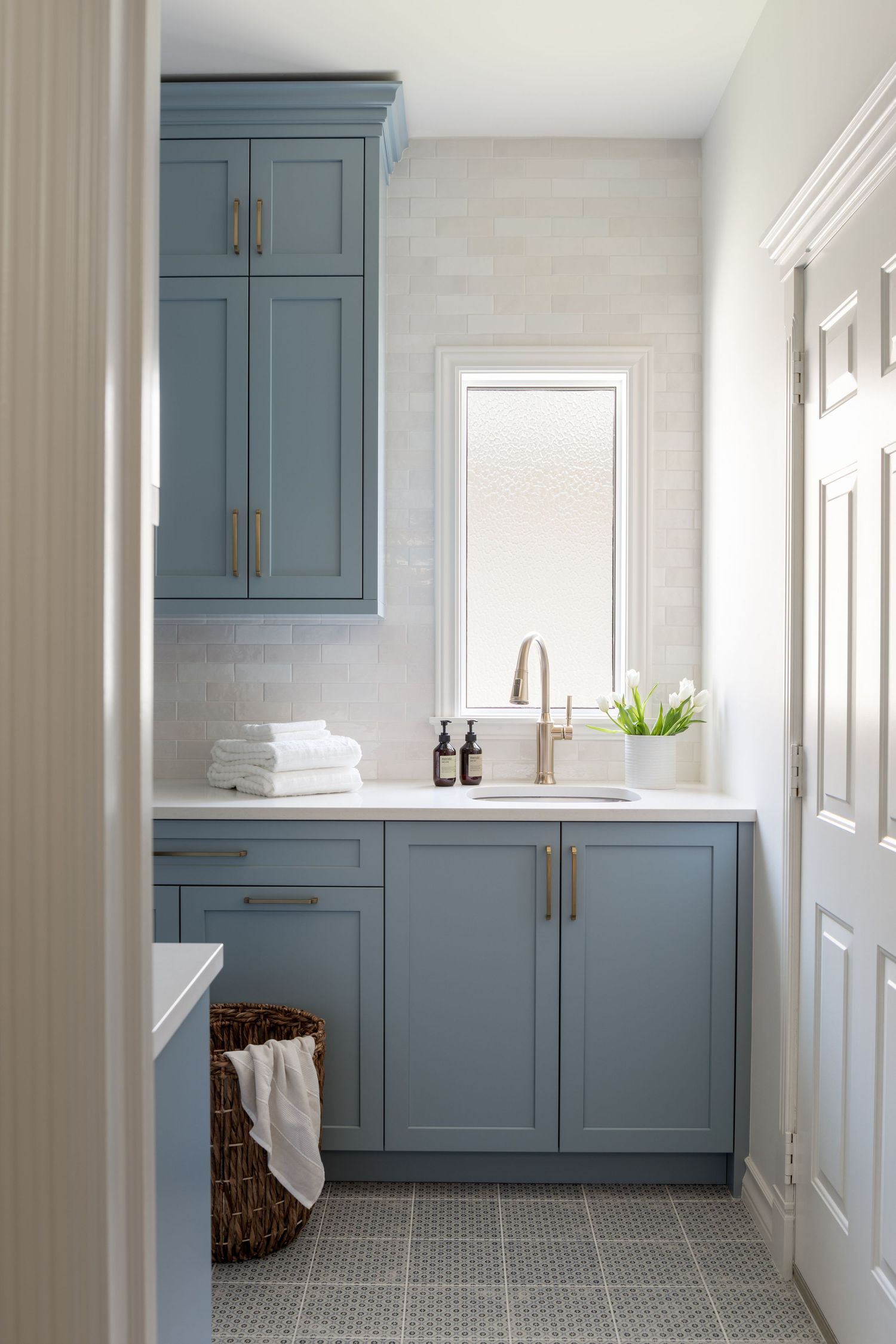 Elegant laundry room with dusty blue shaker cabinets, white quartz countertops, penny tile floor, and rose gold faucet.