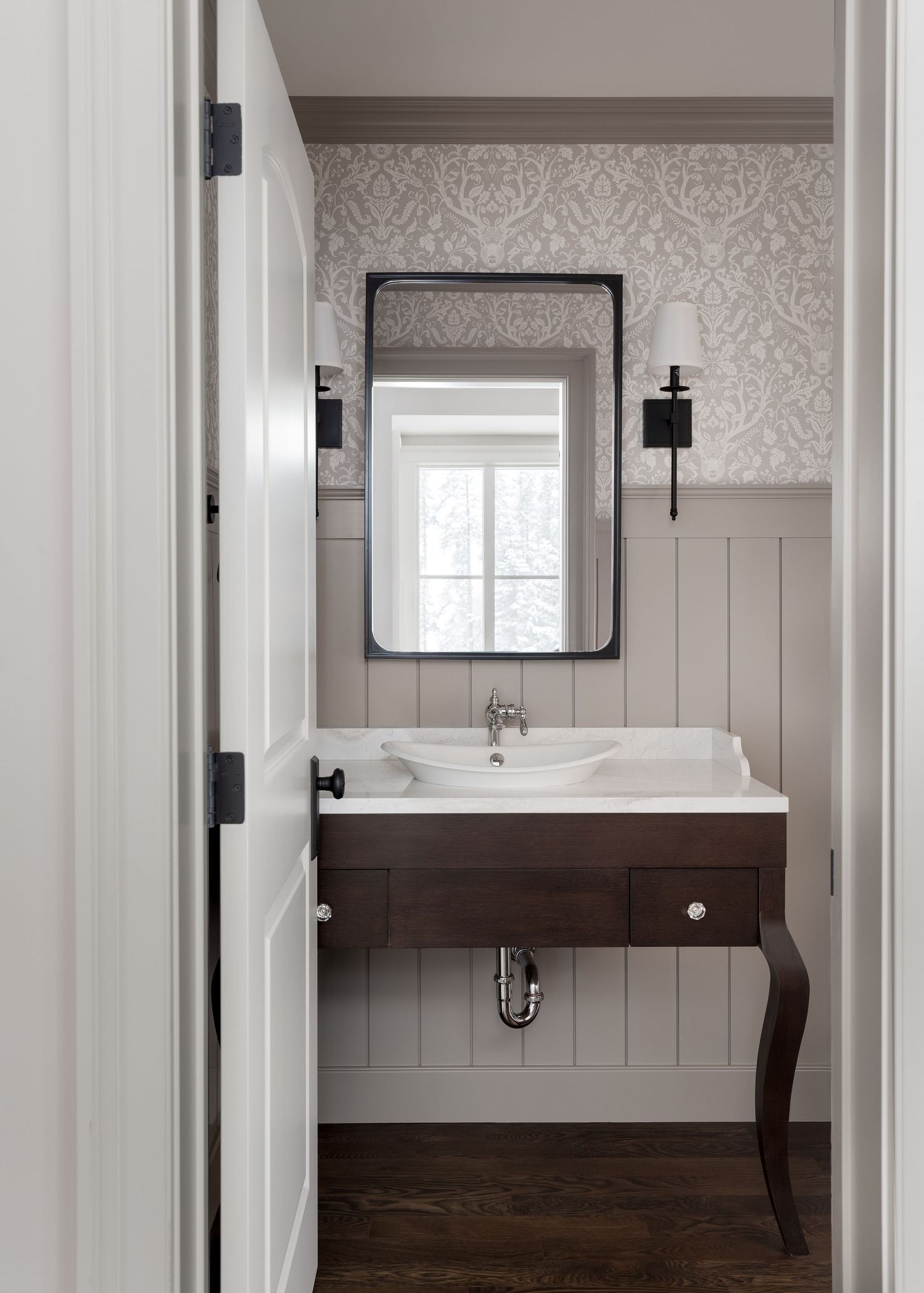 Elegant powder room with damask wallpaper, dark wood floating vanity, wainscoting, and black wall sconces.