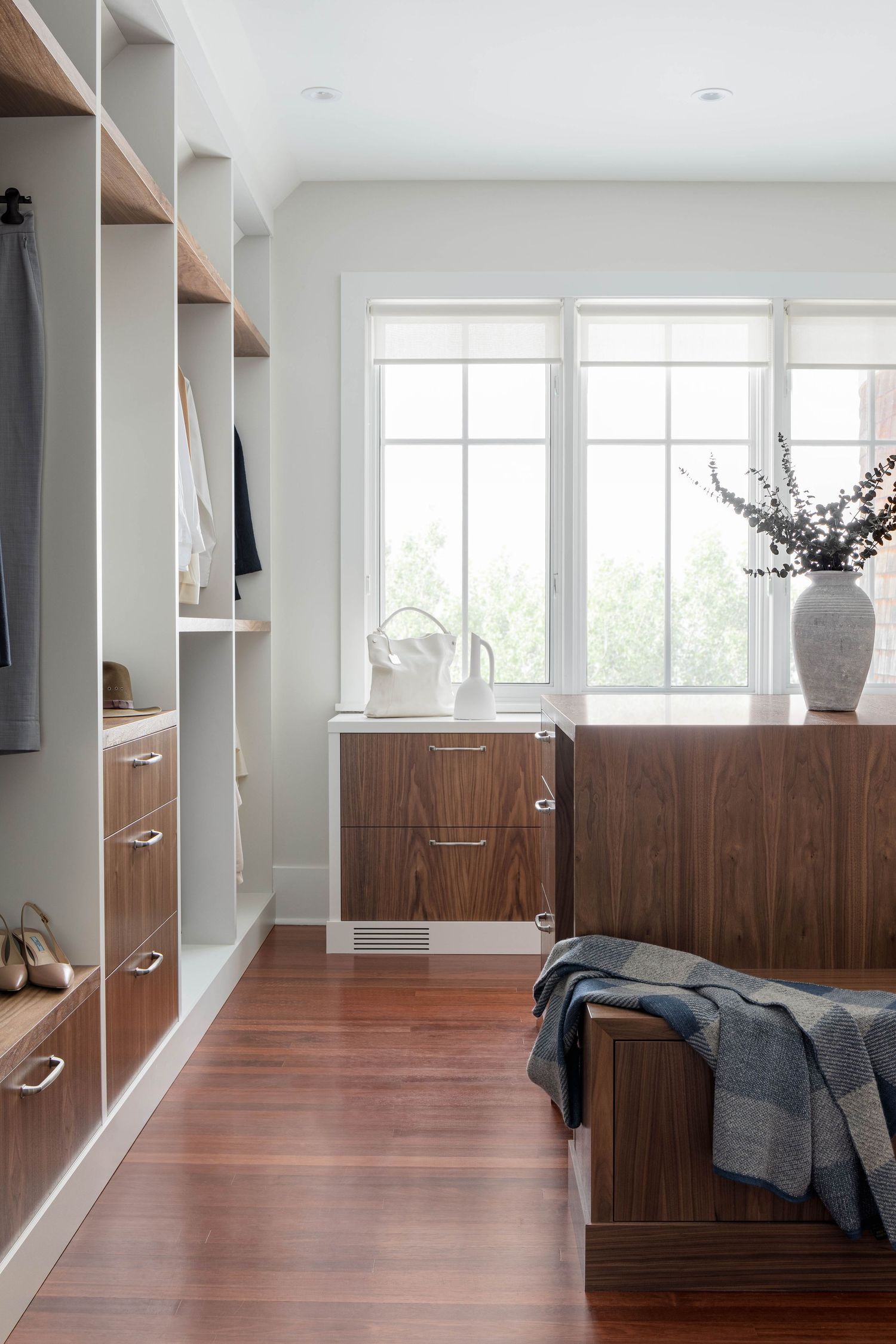 Modern walk-in closet with walnut wood drawers, open shelving, and hardwood floors.