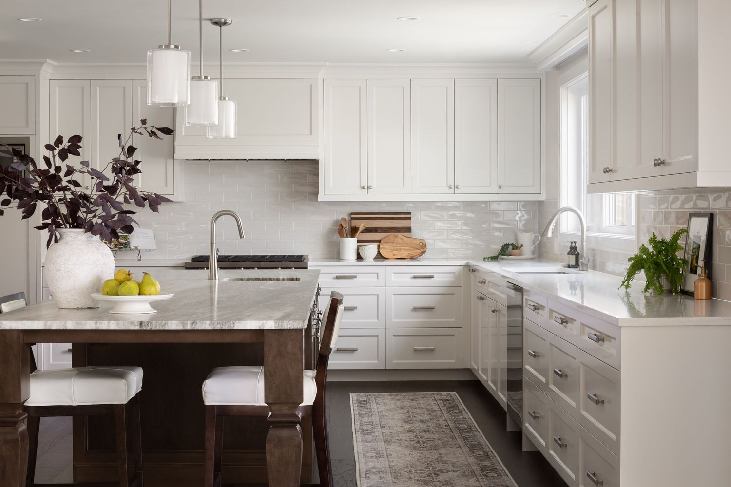Bright white kitchen with shaker cabinets, marble countertops, subway tile backsplash, and a dark wood island with pendant lights.