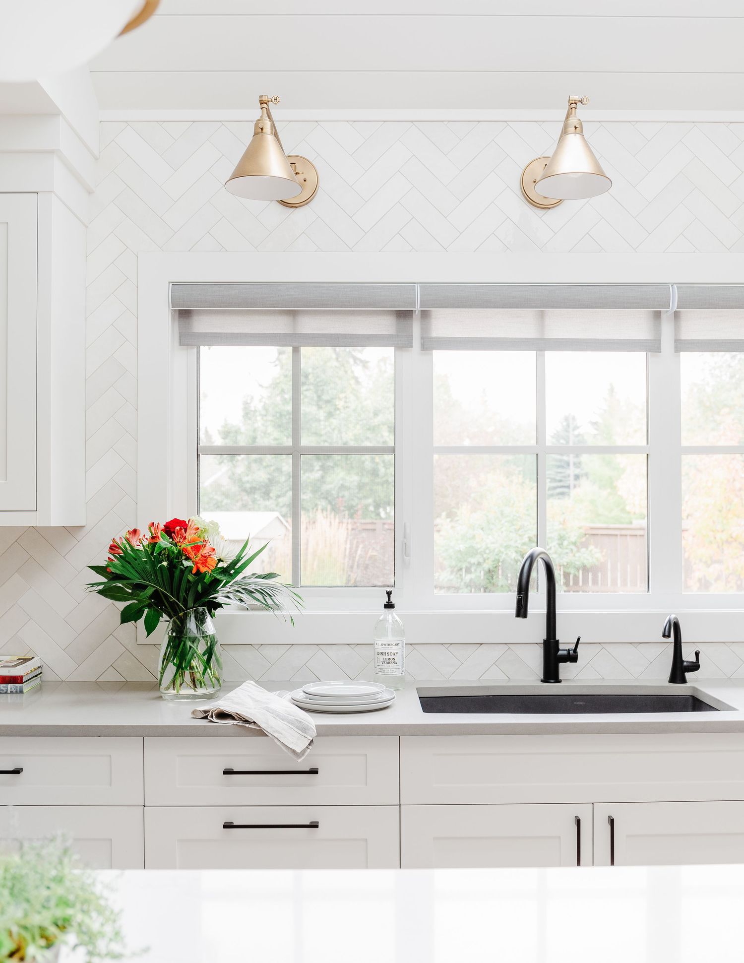 Bright white kitchen with herringbone backsplash, black faucet, undermount sink, and brass wall sconces.