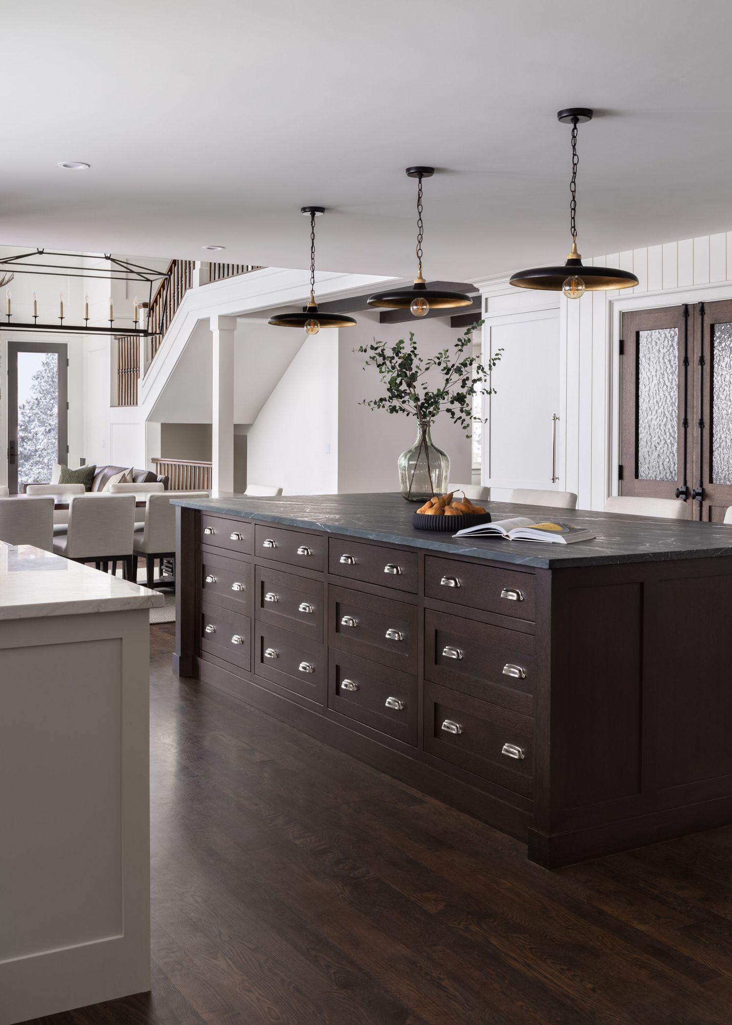Large dark espresso kitchen island with apothecary drawers, slate countertop, and black industrial pendant lights.