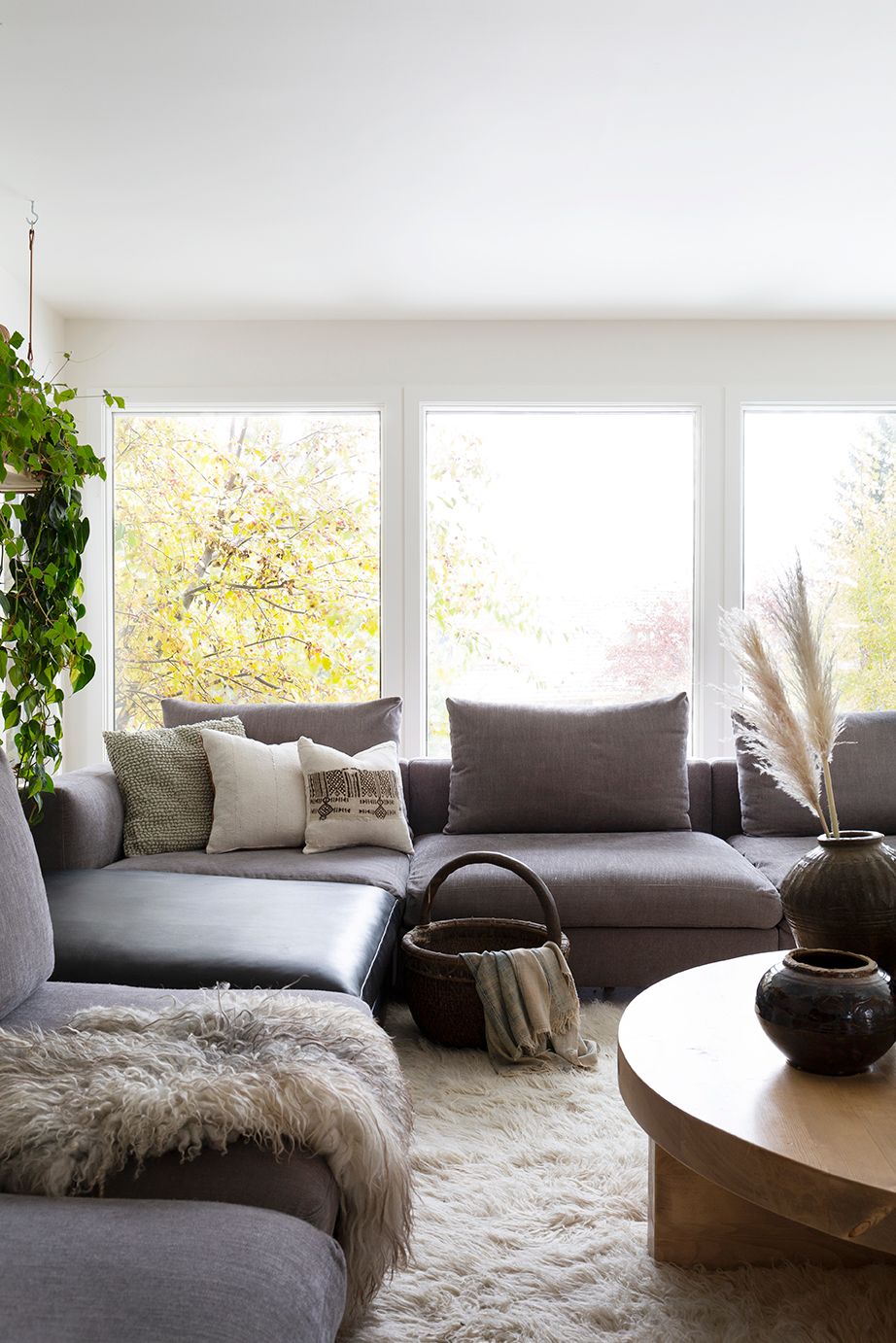Modern living room with gray sectional, shag rug, round wood coffee table, and large windows.