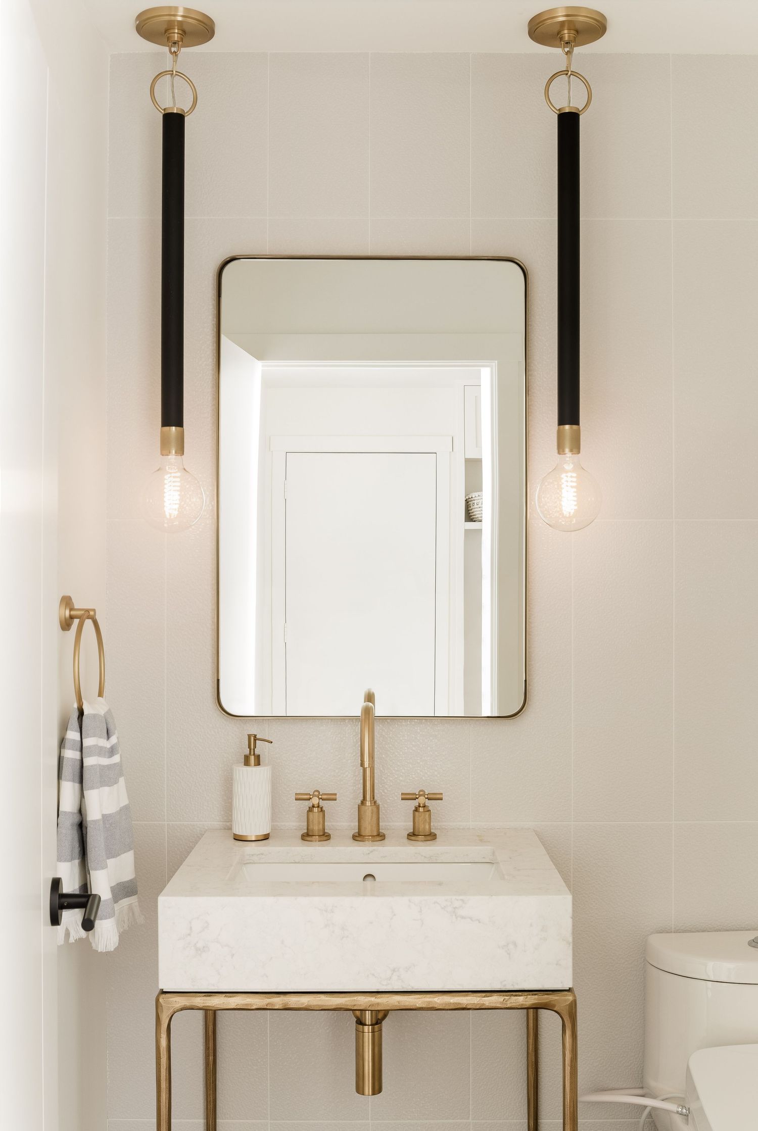 Elegant powder room with brass fixtures, marble vanity, gold-framed mirror, and black pendant lights on white tile walls.