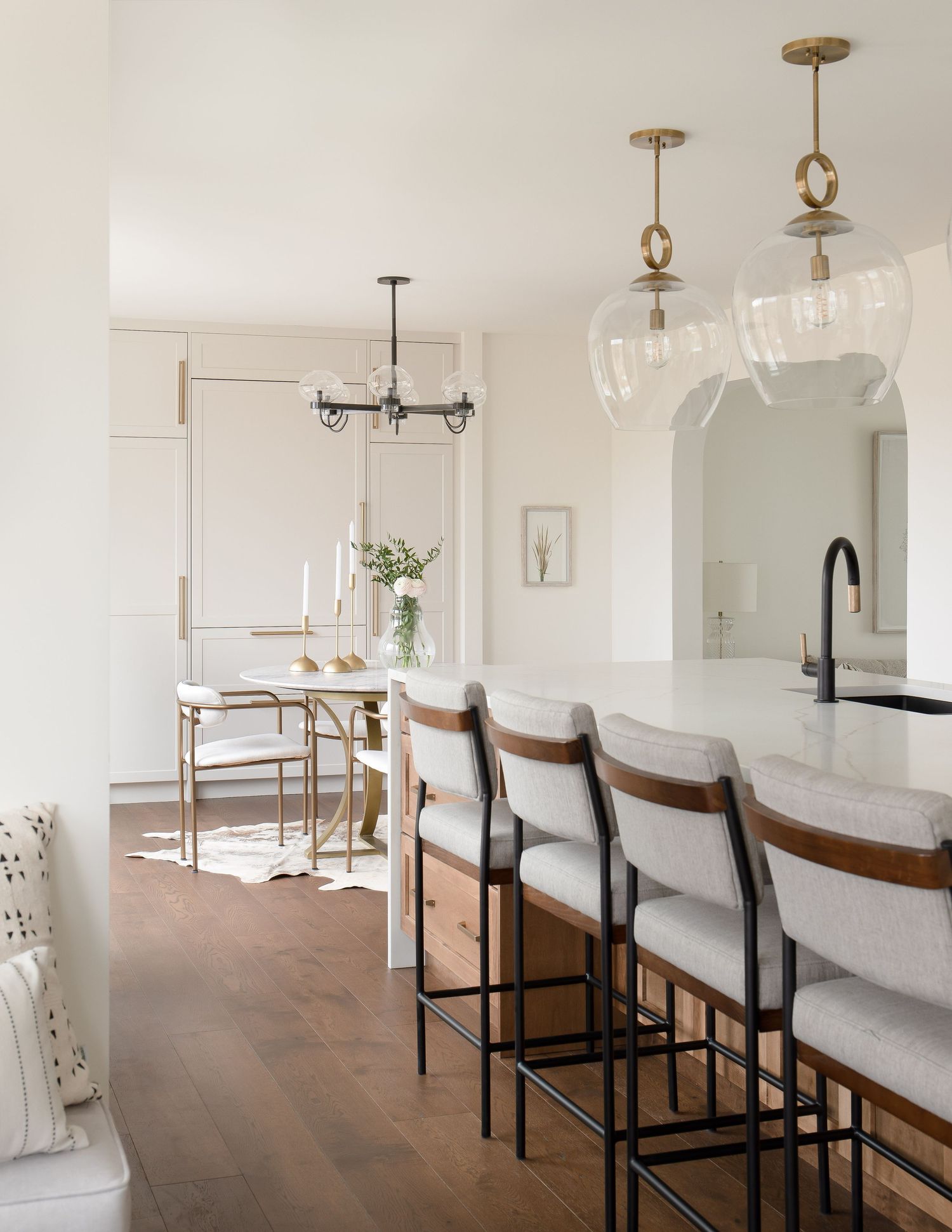 Bright open kitchen with white marble island, glass pendant lights, wood barstools, and herringbone floors.
