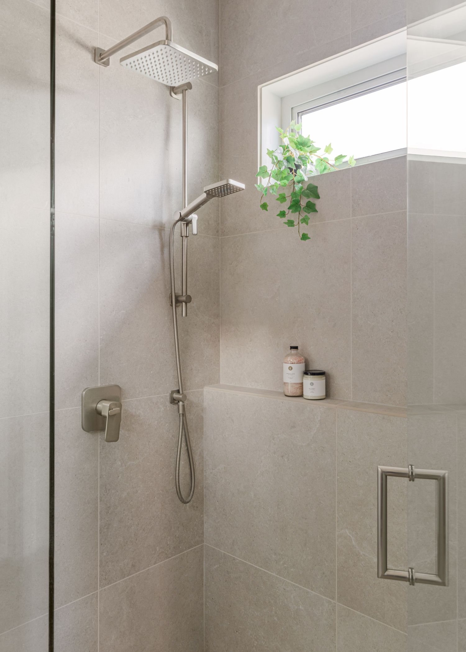 Modern walk-in shower with gray tile, rainfall showerhead, niche shelf, and small window.