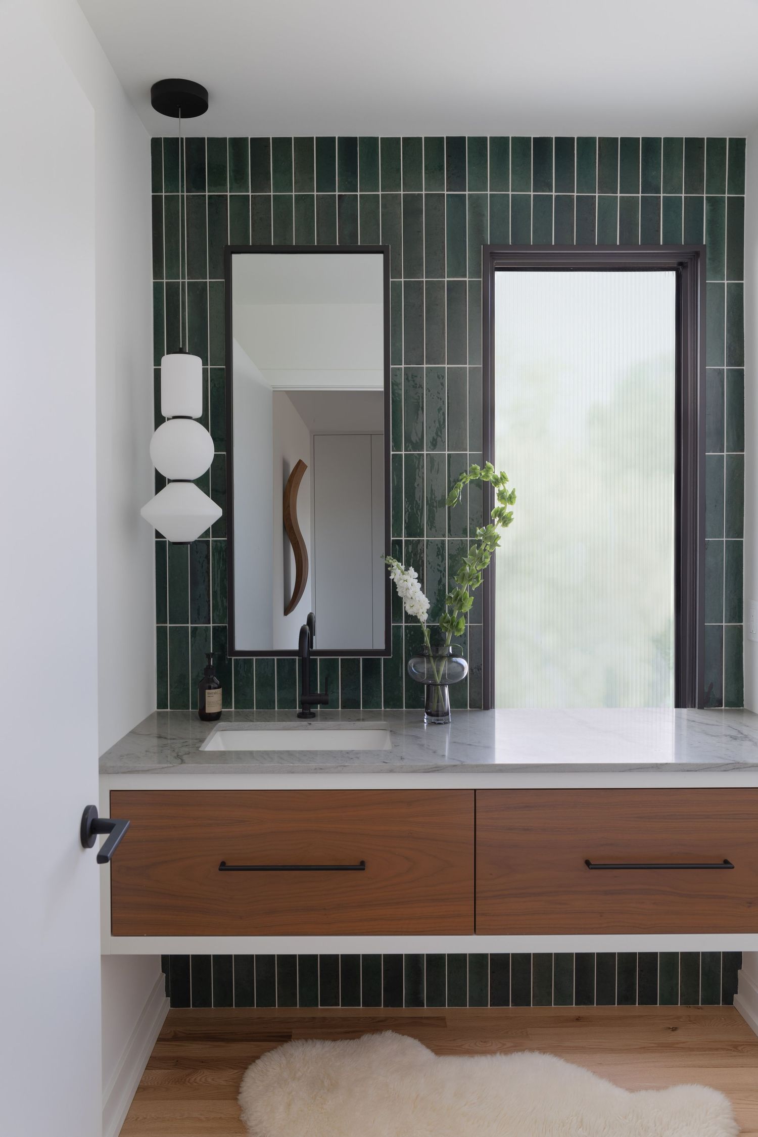 Modern bathroom vanity with green vertical subway tiles, floating walnut cabinet, marble countertop, and arched mirror.