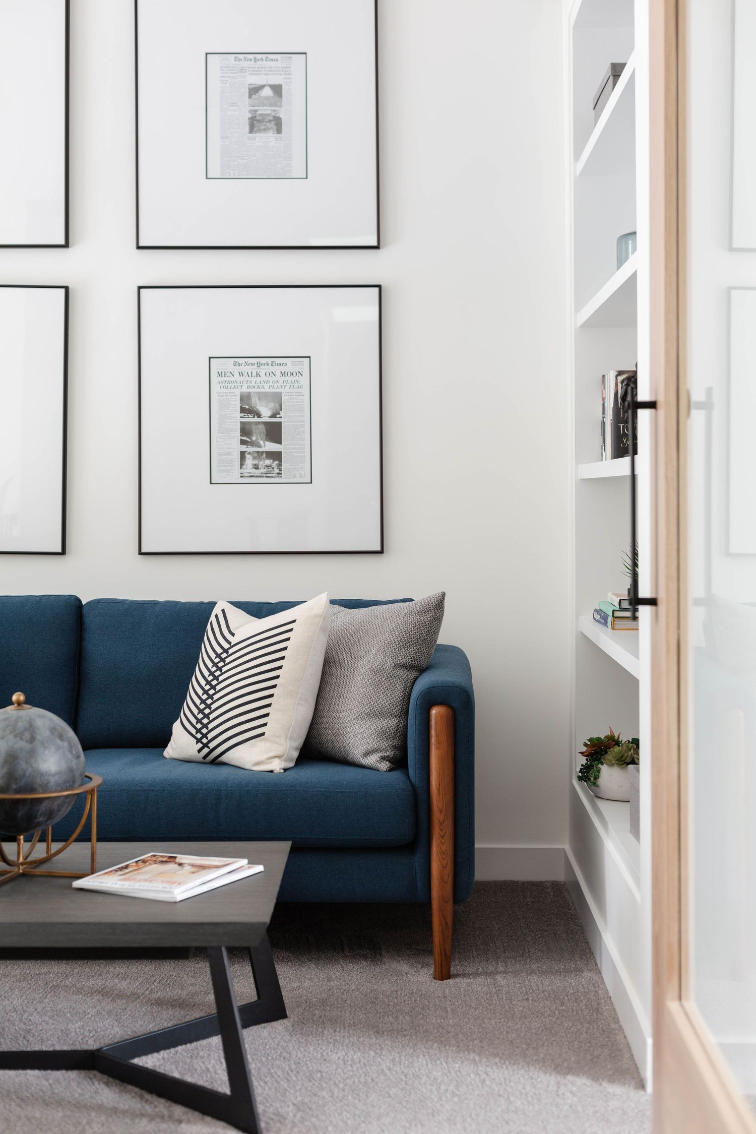 Modern living room with blue sofa, gallery wall frames, and built-in white shelving unit.