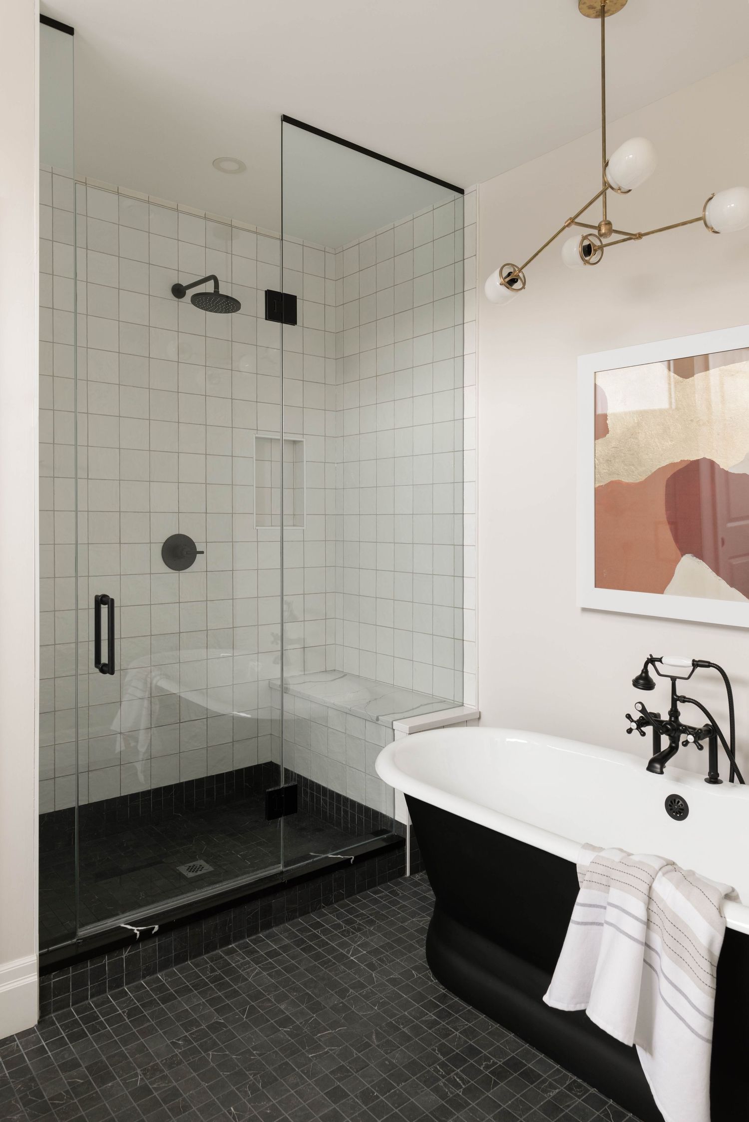 Stylish bathroom with black clawfoot tub, white grid tile shower, dark floor tiles, and brass globe chandelier.